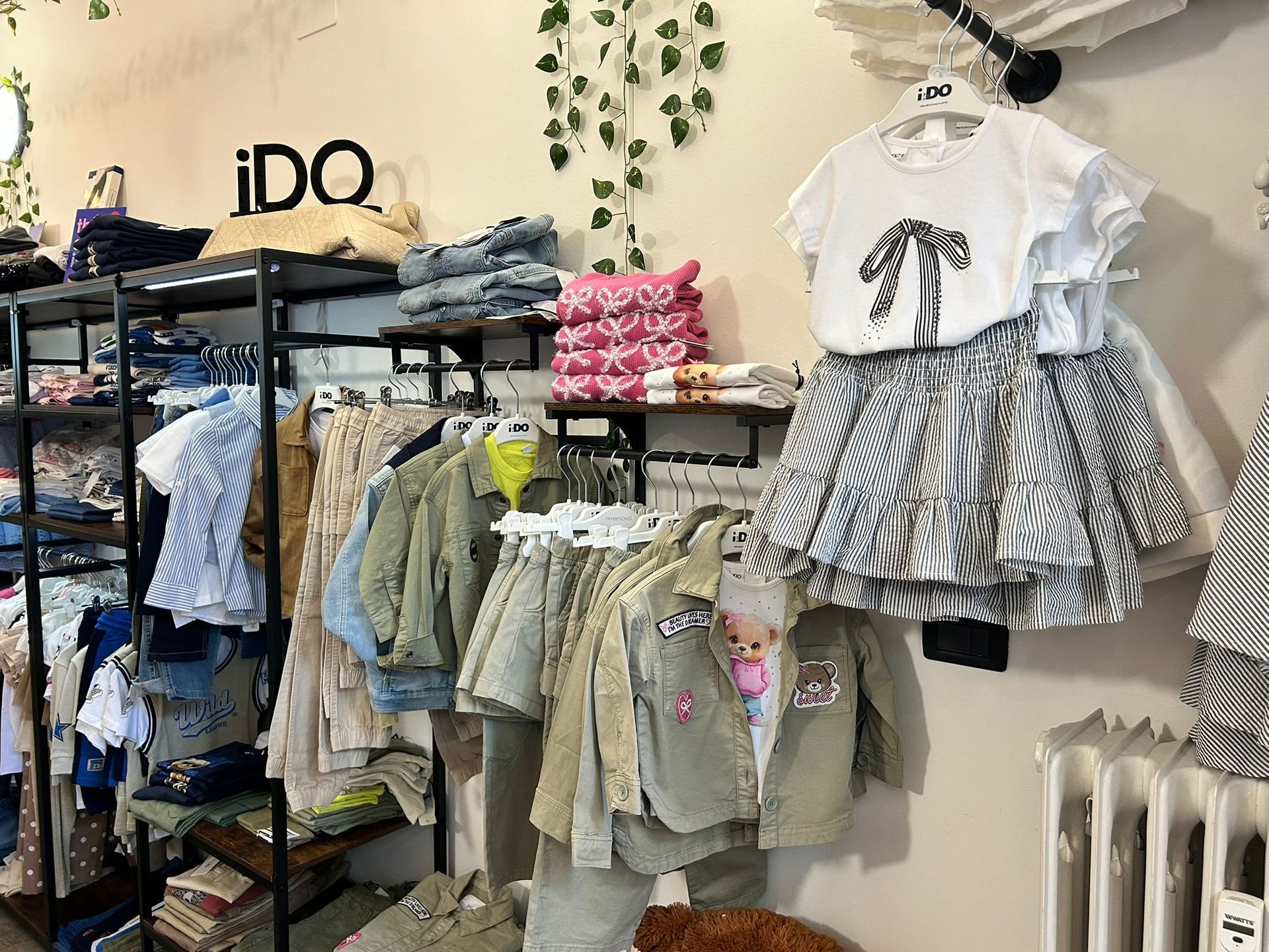 Vetrina di un negozio di abbigliamento per bambini con vestiti, giacche e abiti piegati sugli scaffali.
