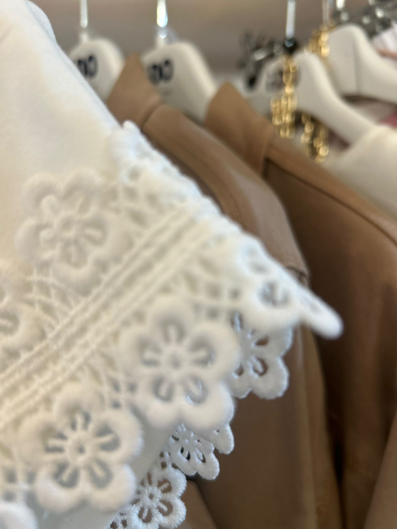 Un capo bianco con bordi di pizzo è appeso a uno stendino, insieme ad altri abiti beige e marrone chiaro su grucce.