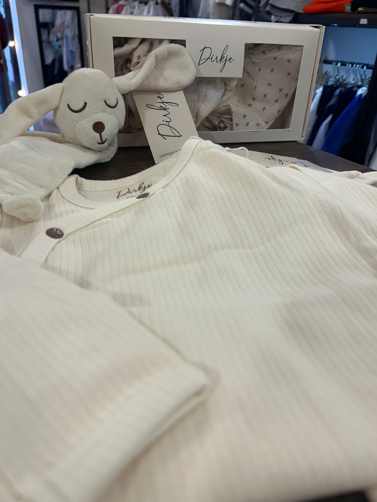 Biancheria da letto a righe bianche con un orsacchiotto di peluche addormentato accanto a una scatola regalo aperta e un biglietto di auguri.