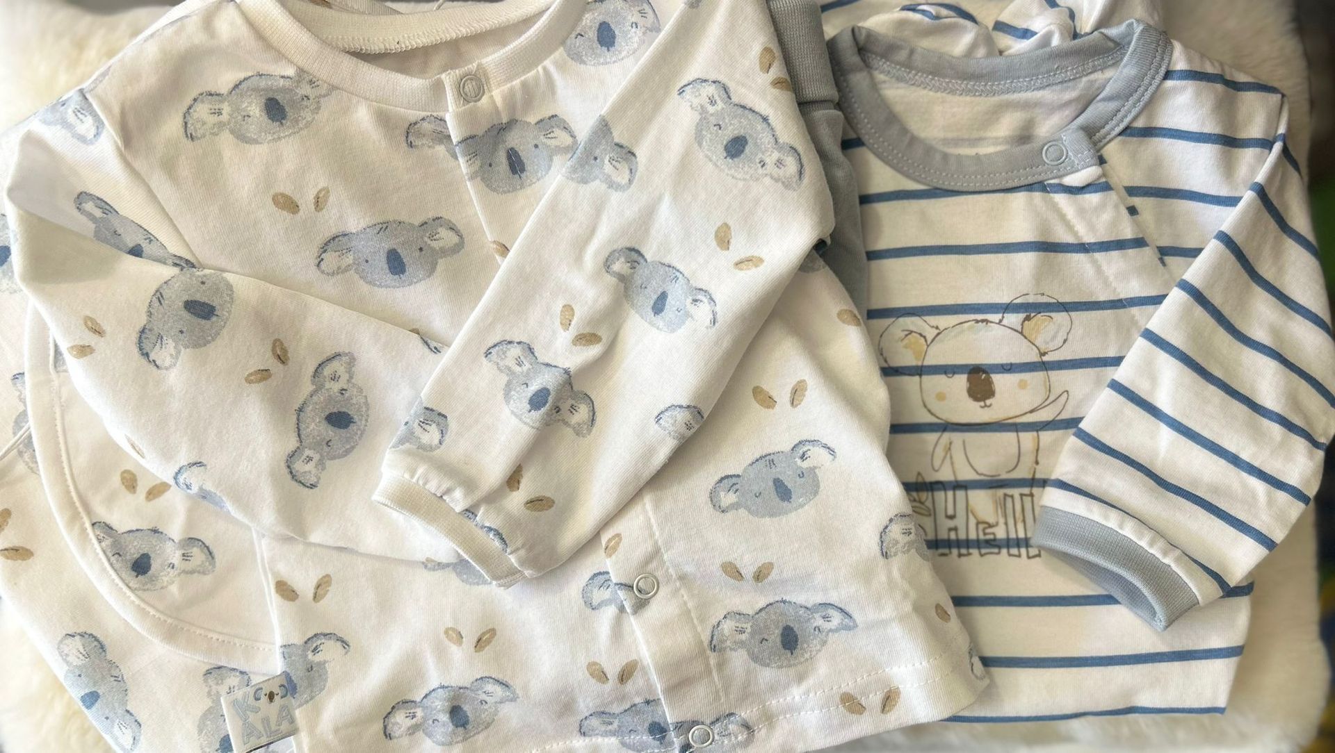Due body per neonati piegati, uno color crema con orsetti e uno bianco con strisce blu, su uno sfondo chiaro.