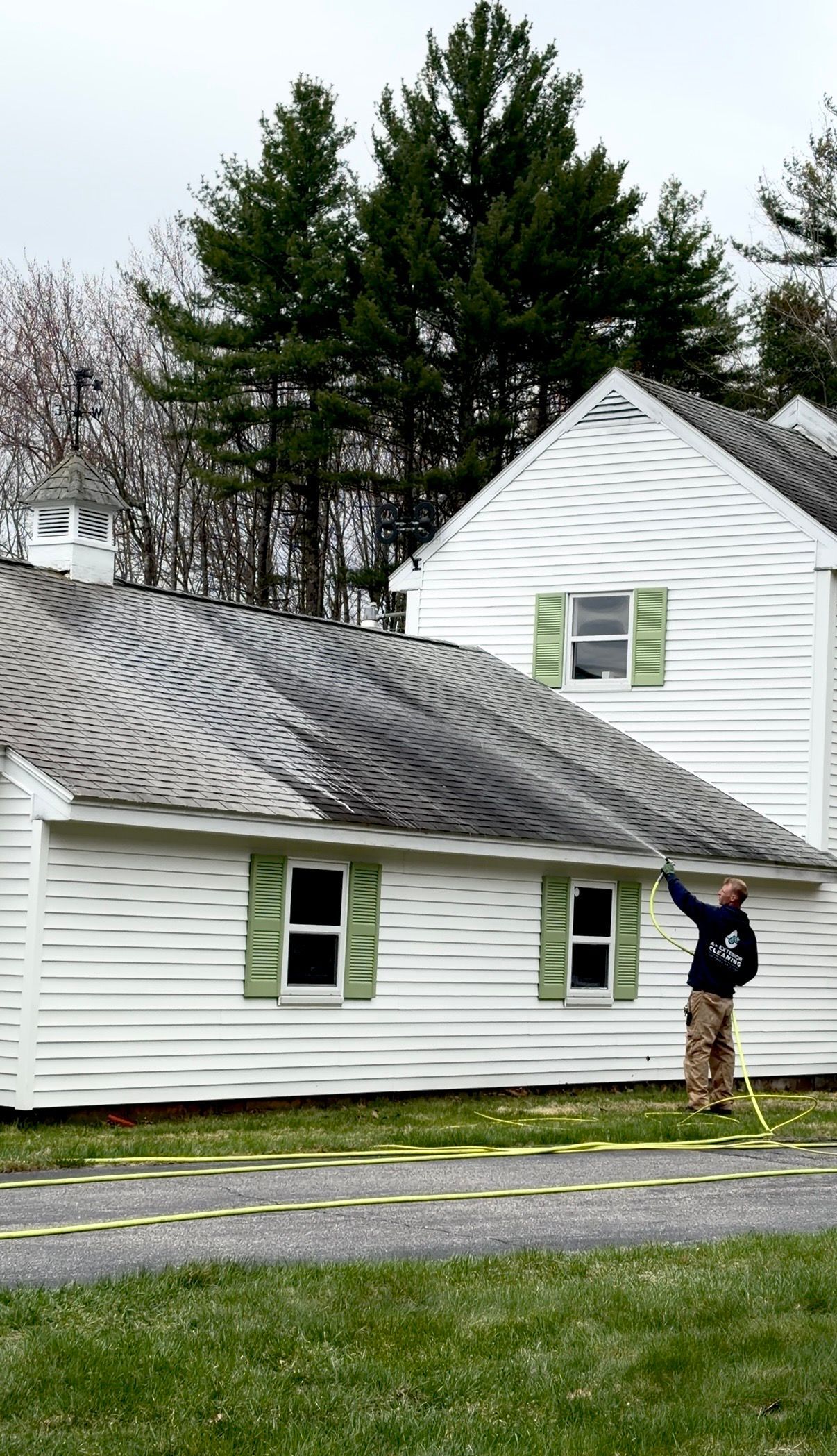 White house with a curved roof and trees behind; a person stands at the front door on a wet day.