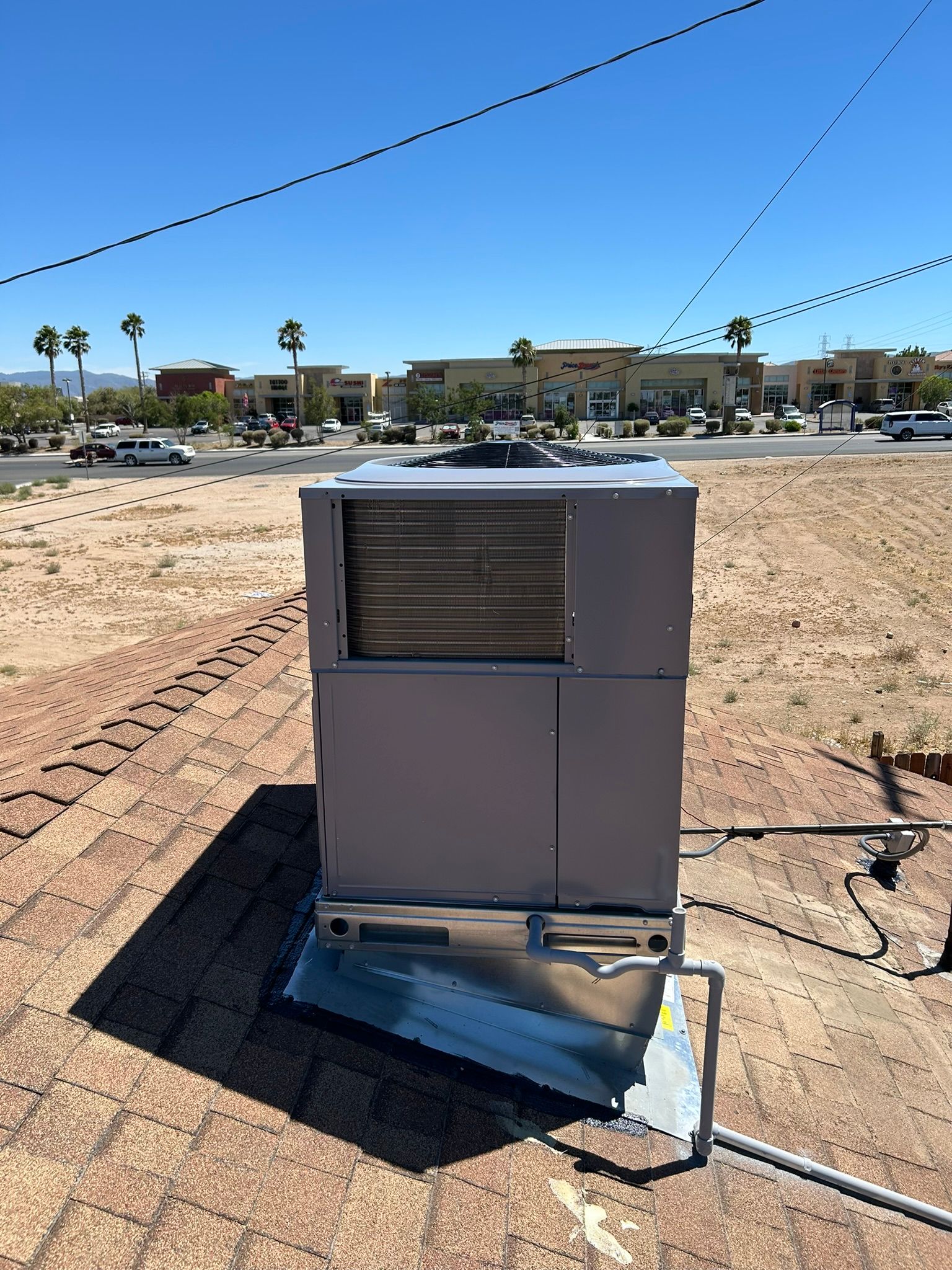 An HVAC unit on a rooftop with a bright sky and commercial buildings in the background.