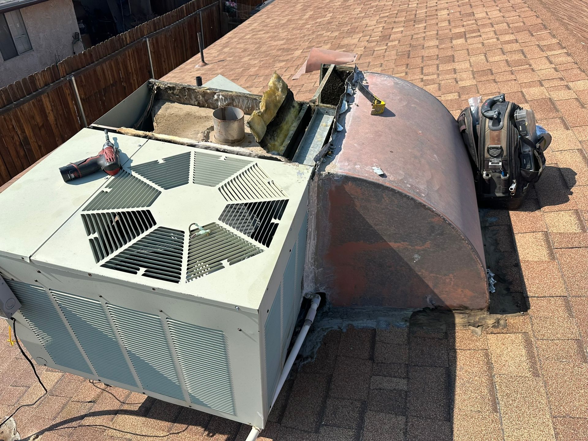 AC unit on a rooftop with open access panel, next to a curved metal hood and tool bag.