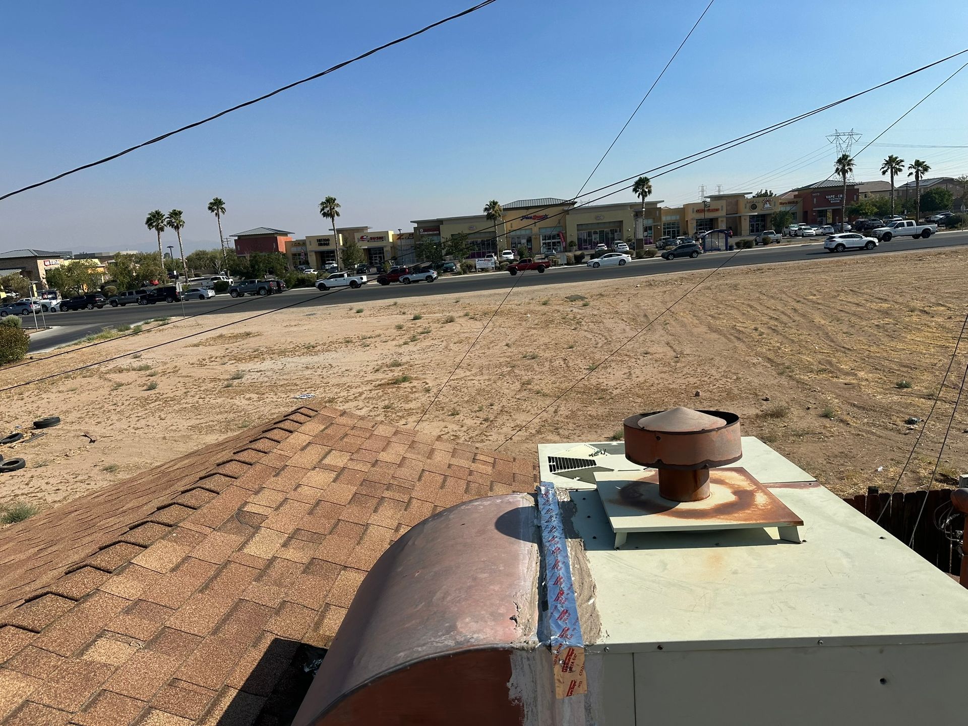 View from a rooftop, looking at a strip mall and desert landscape under a blue sky.