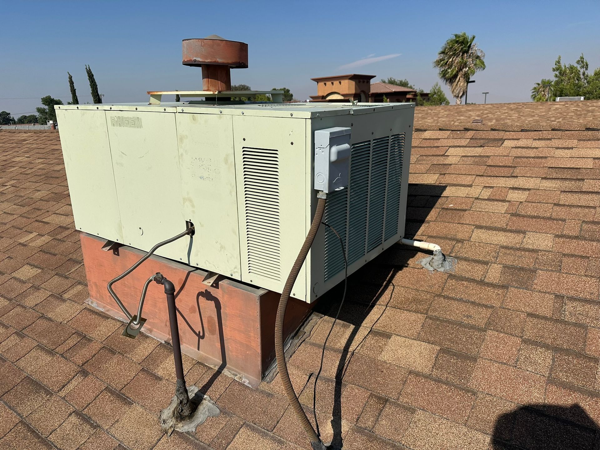 Rooftop air conditioner on a brown-shingled roof under a clear blue sky.