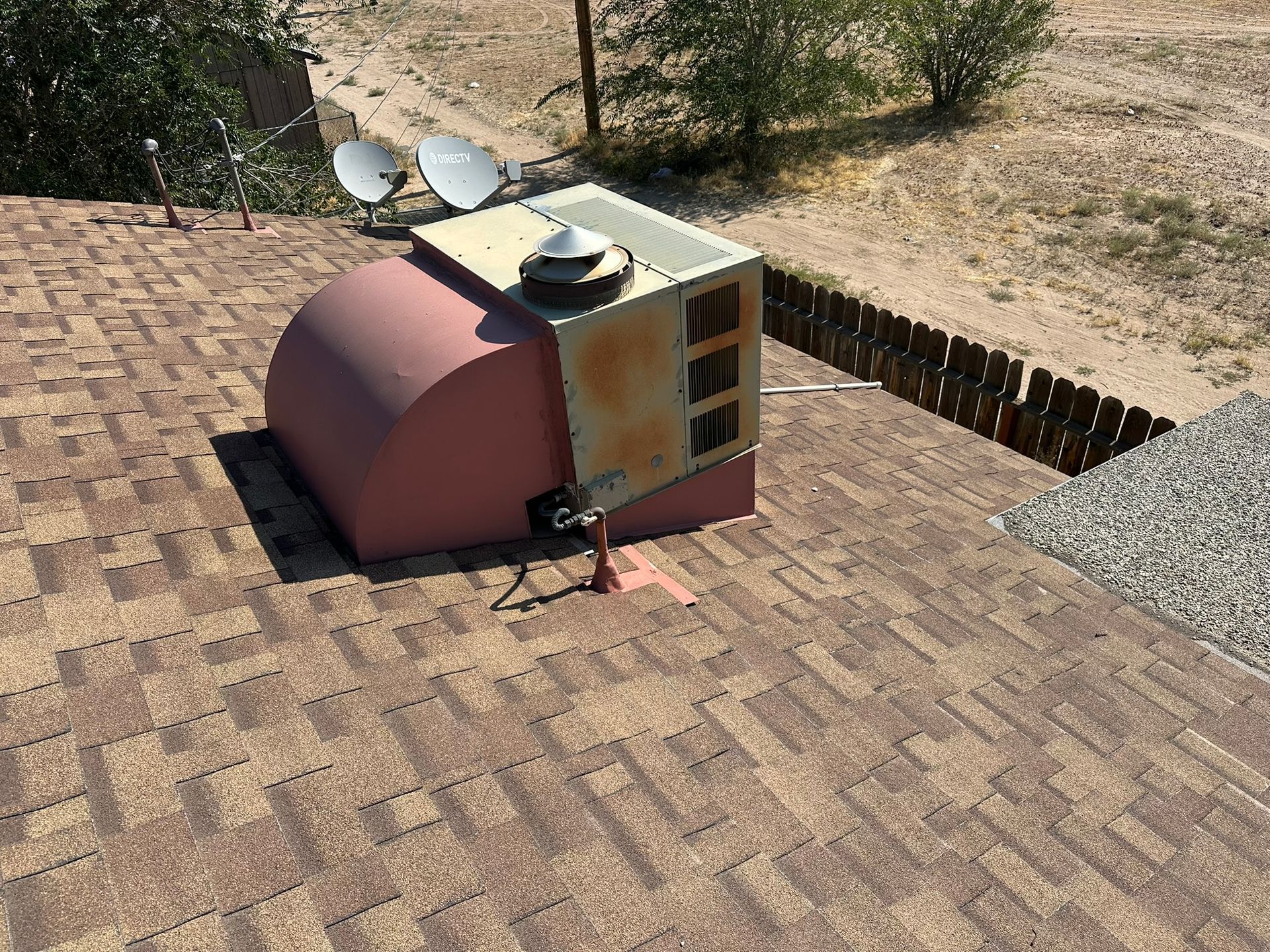 A rooftop HVAC unit with satellite dishes, on a brown shingled roof, outdoors.
