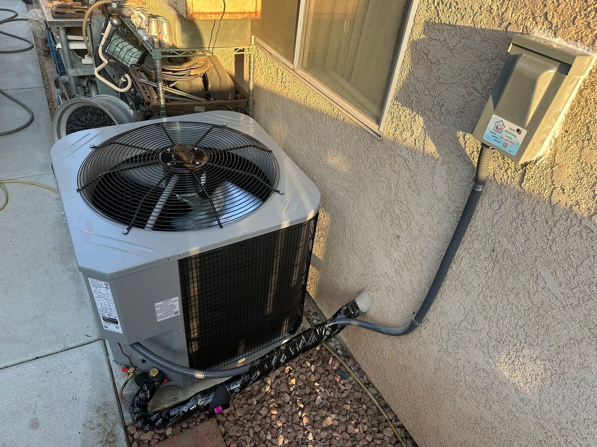 Exterior air conditioning unit next to a stucco wall, connected to an electrical box.