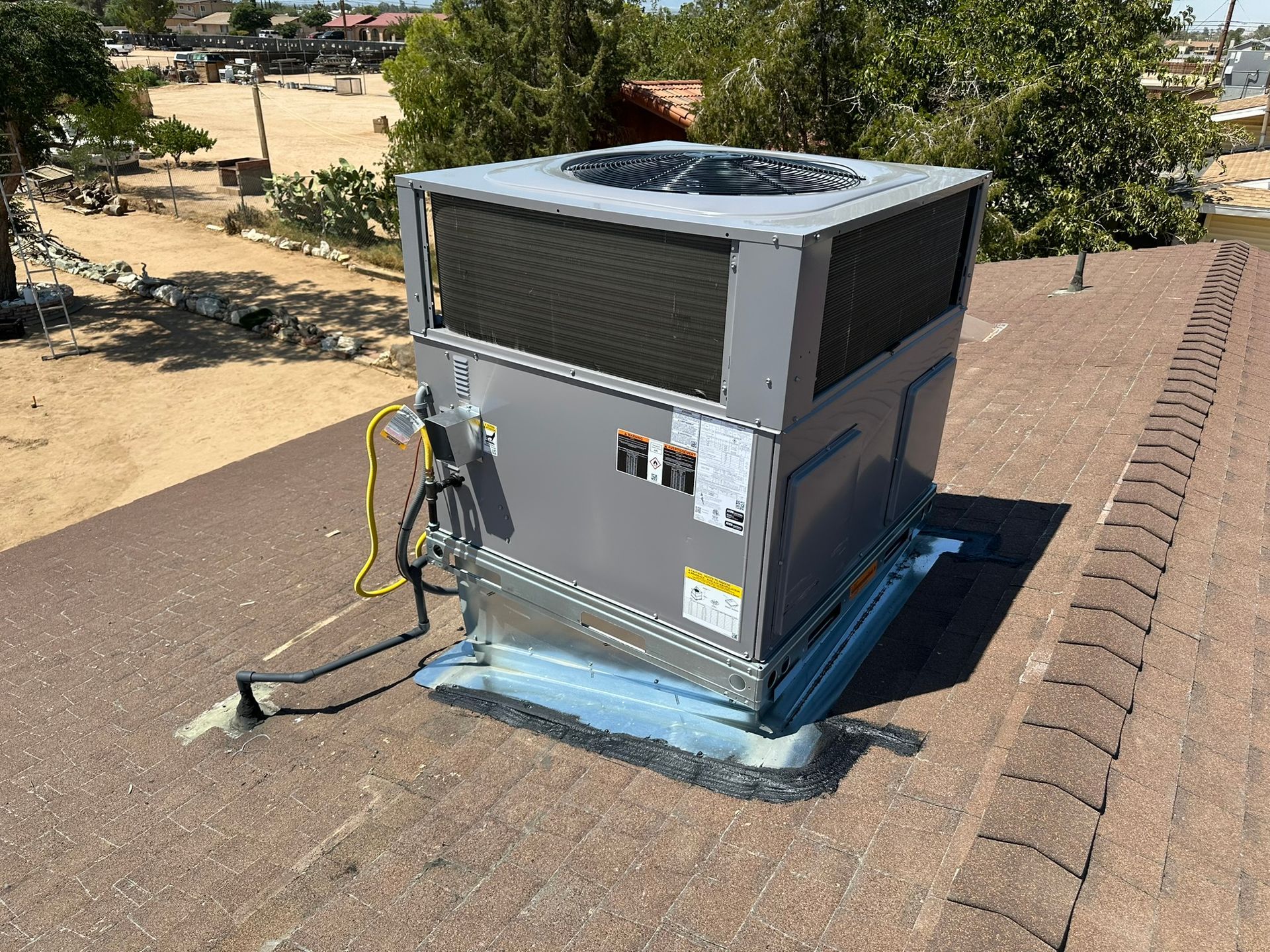 Rooftop HVAC unit, gray and silver, on a brown shingled roof, with wiring visible.