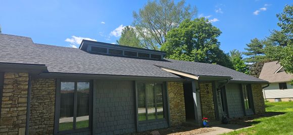 Close-up of a house roof with gray shingles, dark metal roof, and white trim with a gutter.