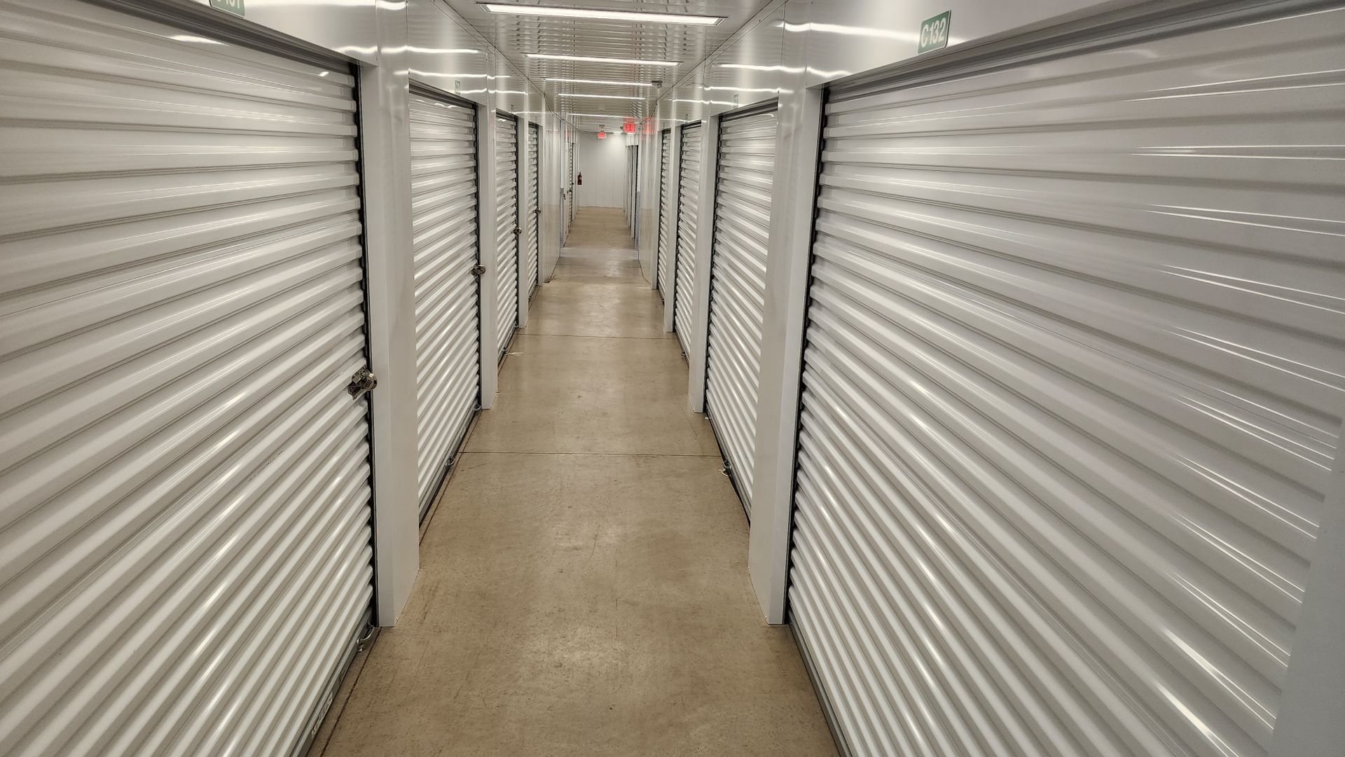 Interior view of a storage unit facility hallway with closed, white metal doors lining both sides.