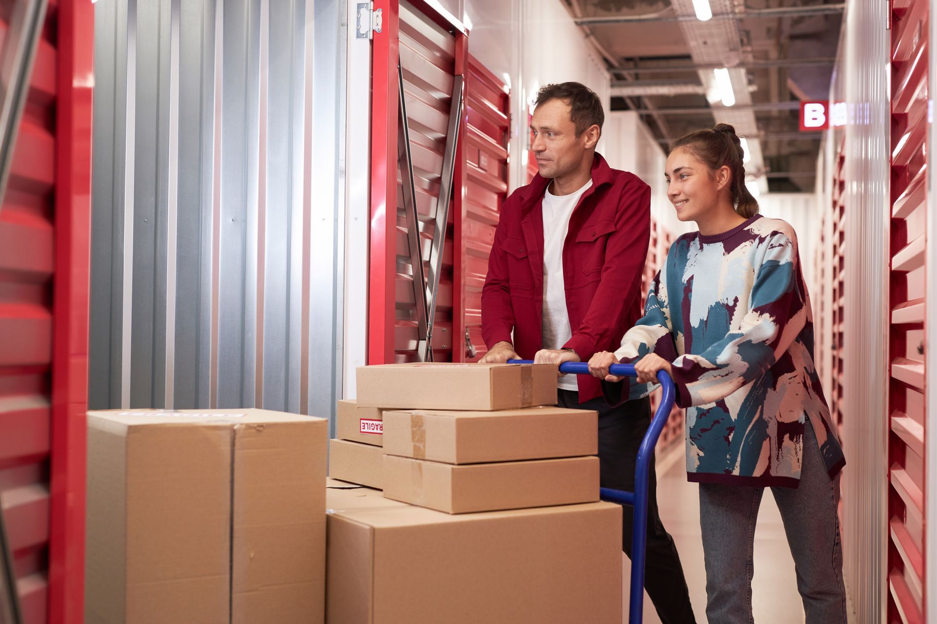 Couple moving boxes on a cart into a climate-controlled storage unit