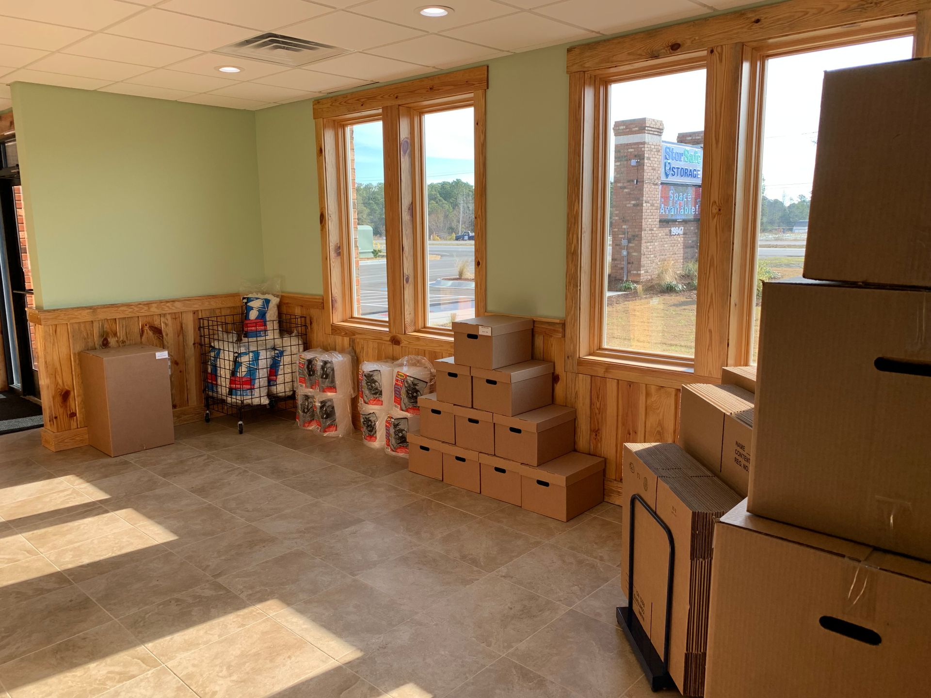 Interior of a room with boxes and items near windows; a street and building are visible outside.