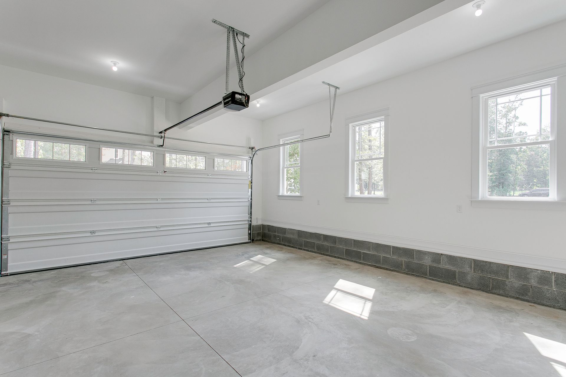 Empty white garage with gray concrete floor, garage door, and windows.