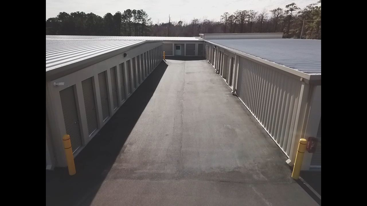 Exterior of a storage facility with units lining both sides of an asphalt walkway under a bright sky.