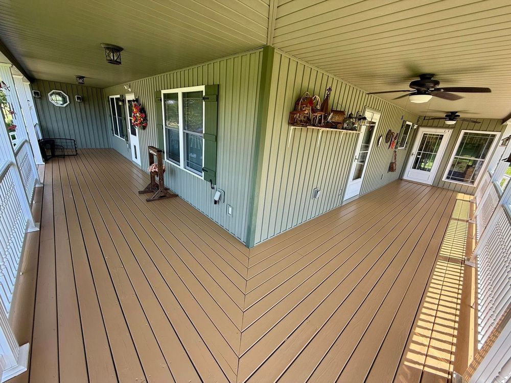 Covered front porch with tan deck, white siding, windows, ceiling fans, and hanging plants