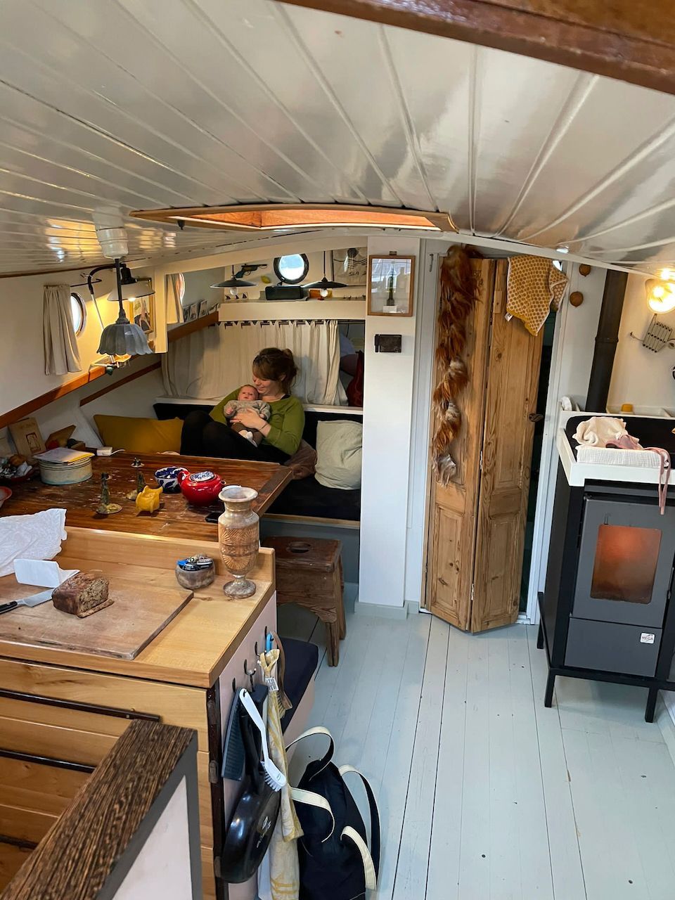 Gezellig interieur van een tiny house met houten aanrechtbladen, een persoon aan tafel en een houtkachel tegen de muur.