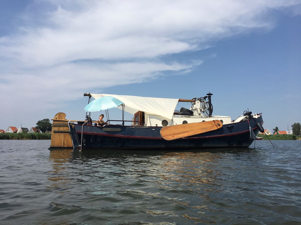 Een klein bootje met een overkapping drijft op kalm water onder een bewolkte hemel.