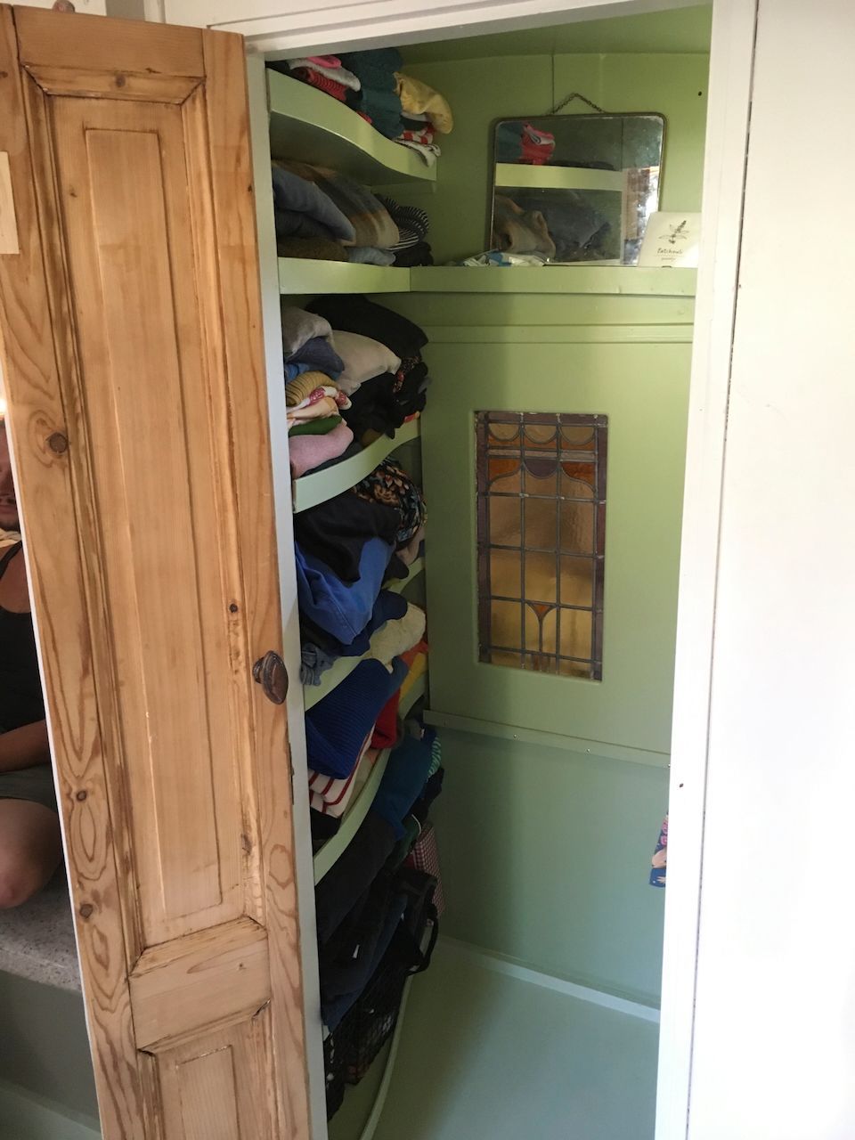 Open houten kast met groene wanden en planken vol opgevouwen kleding en linnengoed.