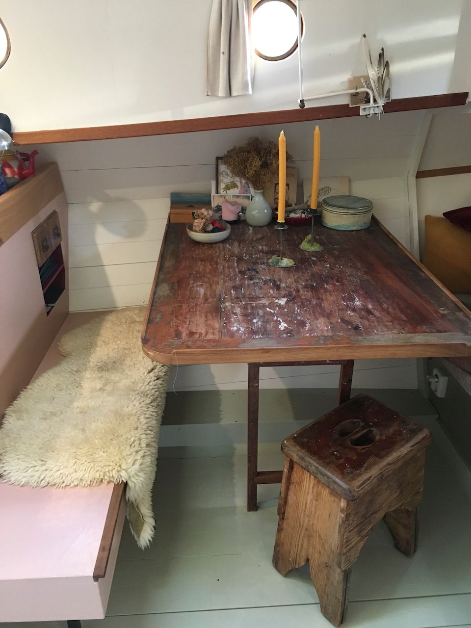 Een knusse eethoek met een houten tafel, twee stoelen, kaarsen en een plank onder het raam.