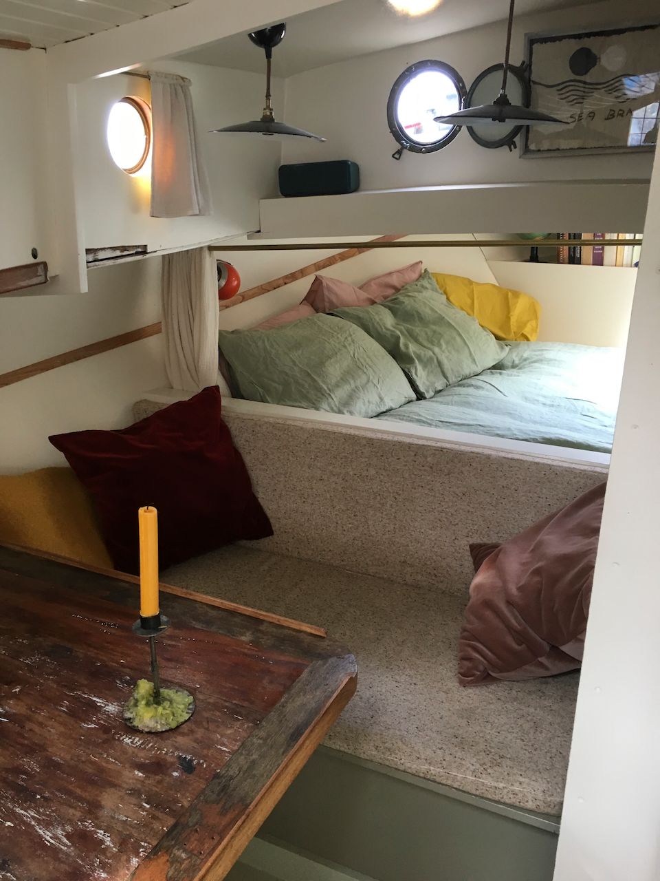 Gezellige slaaphoek op de mezzanine met bed, kussens, hanglampen en een rustieke houten tafel op de voorgrond.