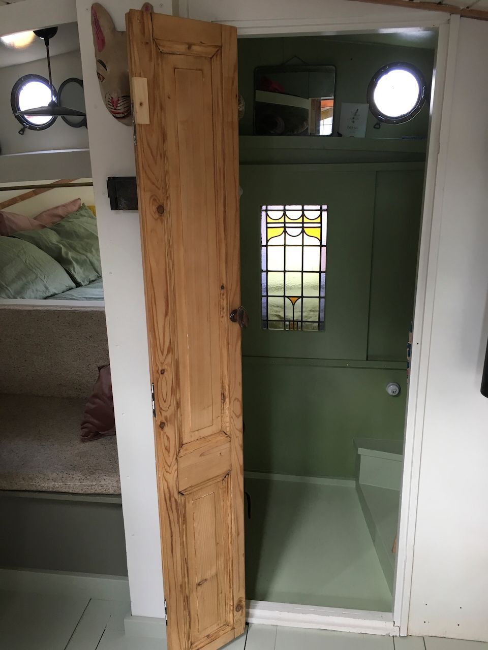 Een open houten deur onthult een kleine groene kamer met ronde ramen en een raam van glas met een patroon.