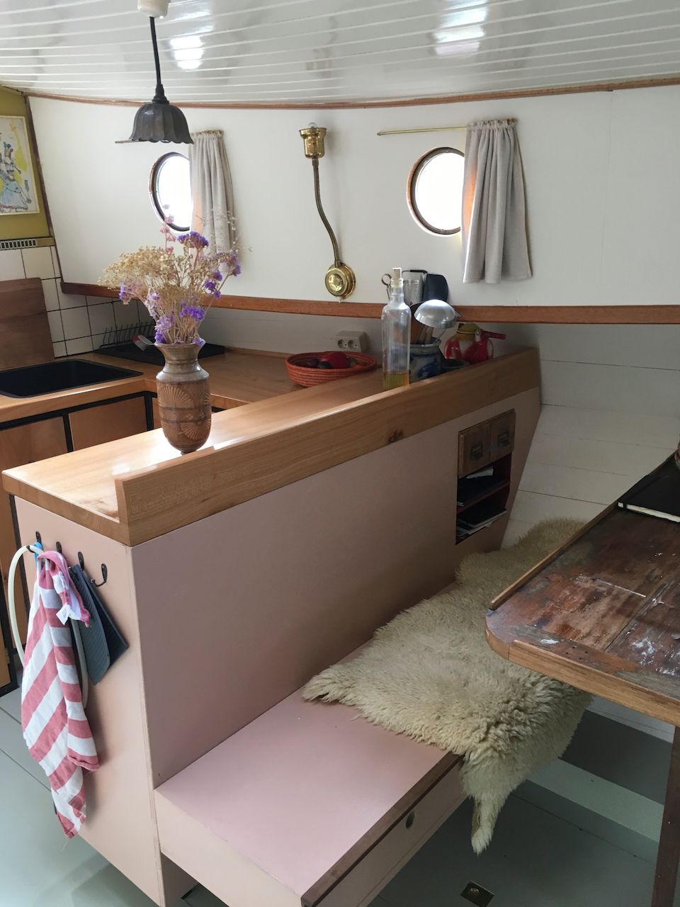 Gezellige kitchenette in een blokhut met roze aanrechtbladen, houten afwerking, een klein bankje en een vaas met bloemen.