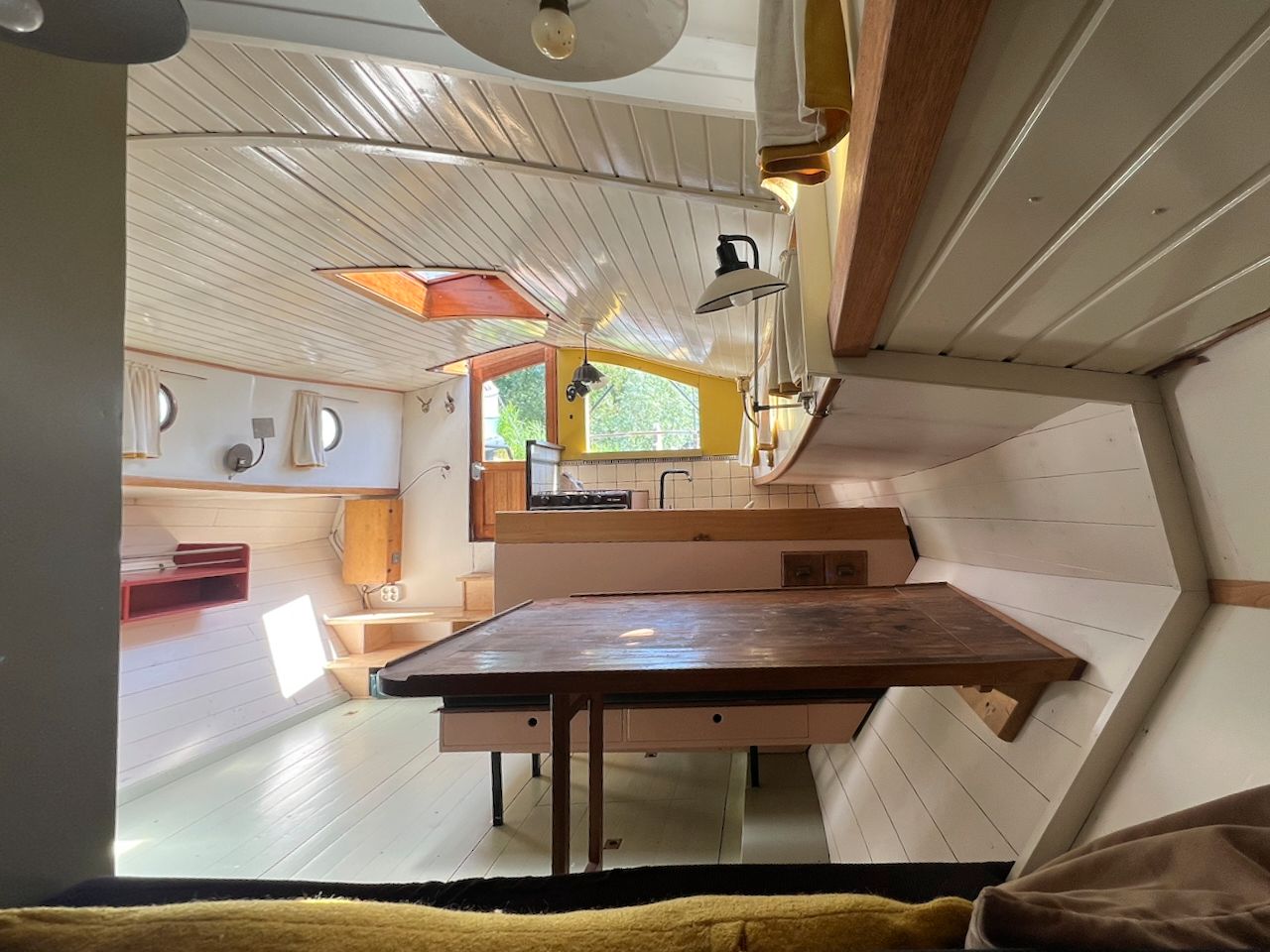 Gezellig café-interieur met houten tafels, witte muren en een groot raam dat daglicht binnenlaat.