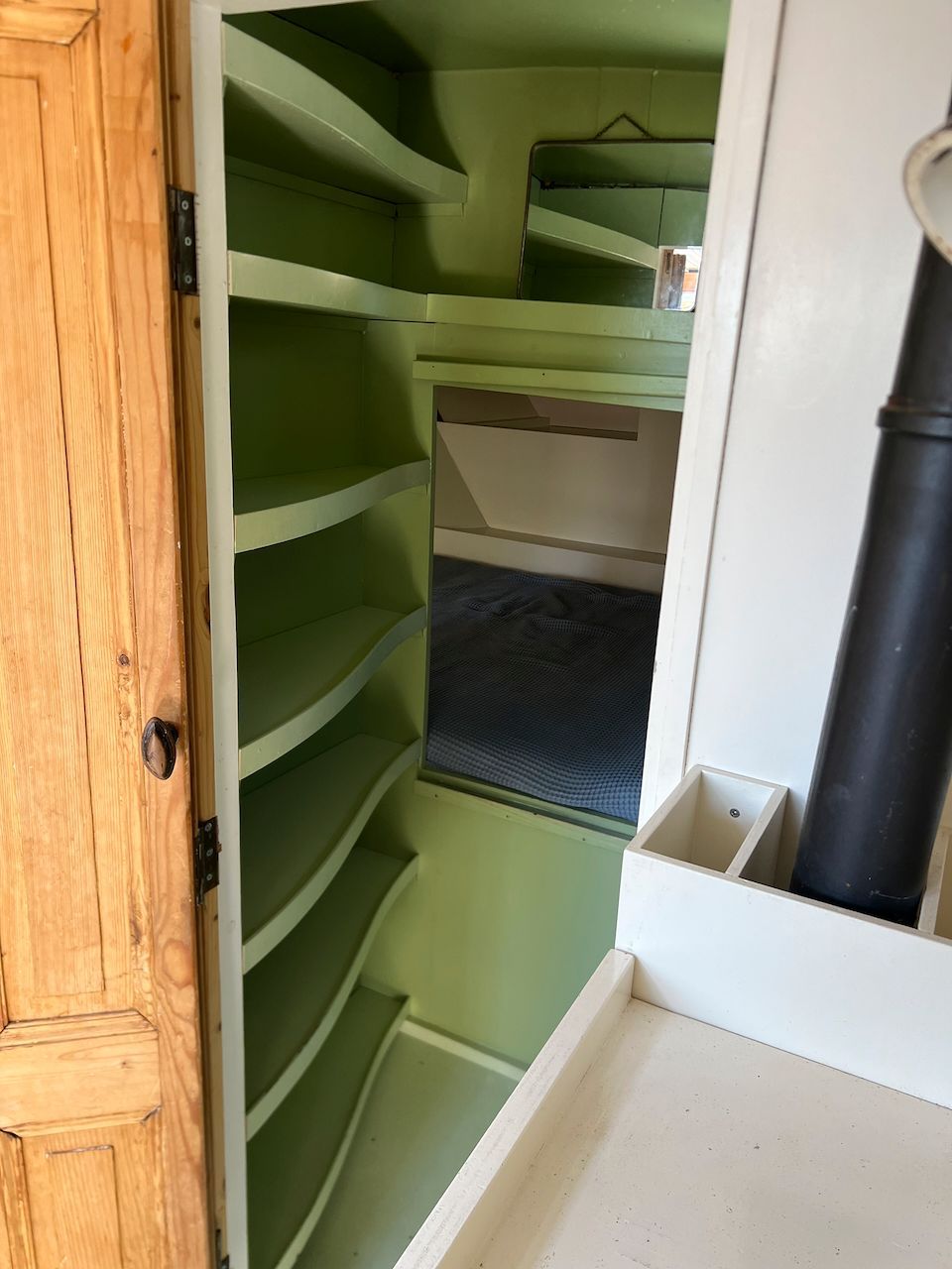 Groene inbouwplanken in een smalle kast of voorraadkast met een houten deur.