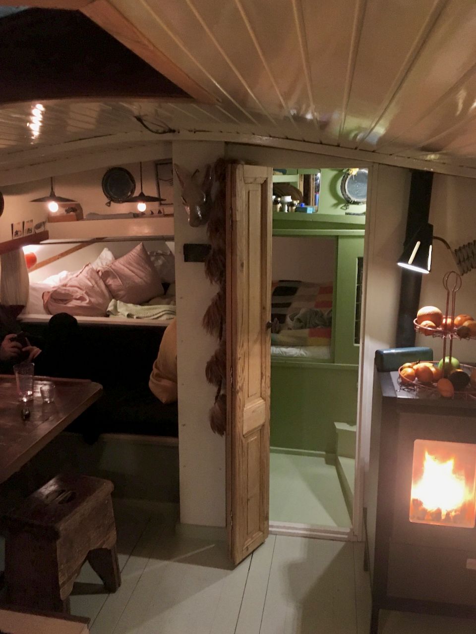 Gezellig camperinterieur met hoogslaper, groene kast, smalle gang en een warme houtkachel.