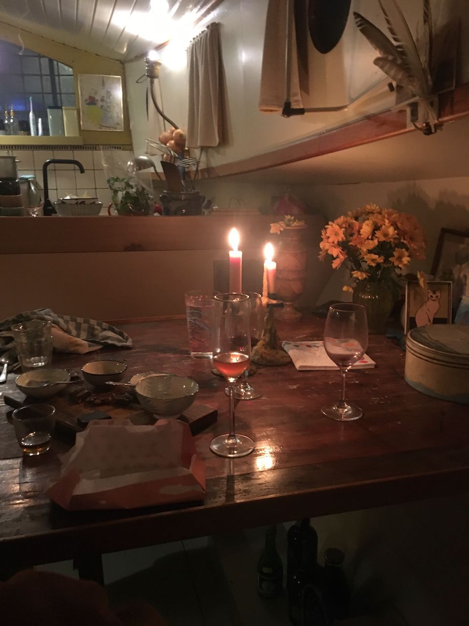 Een schemerig tafeltje met brandende kaarsen, glaswerk, bloemen en borden in een gezellige binnenruimte.