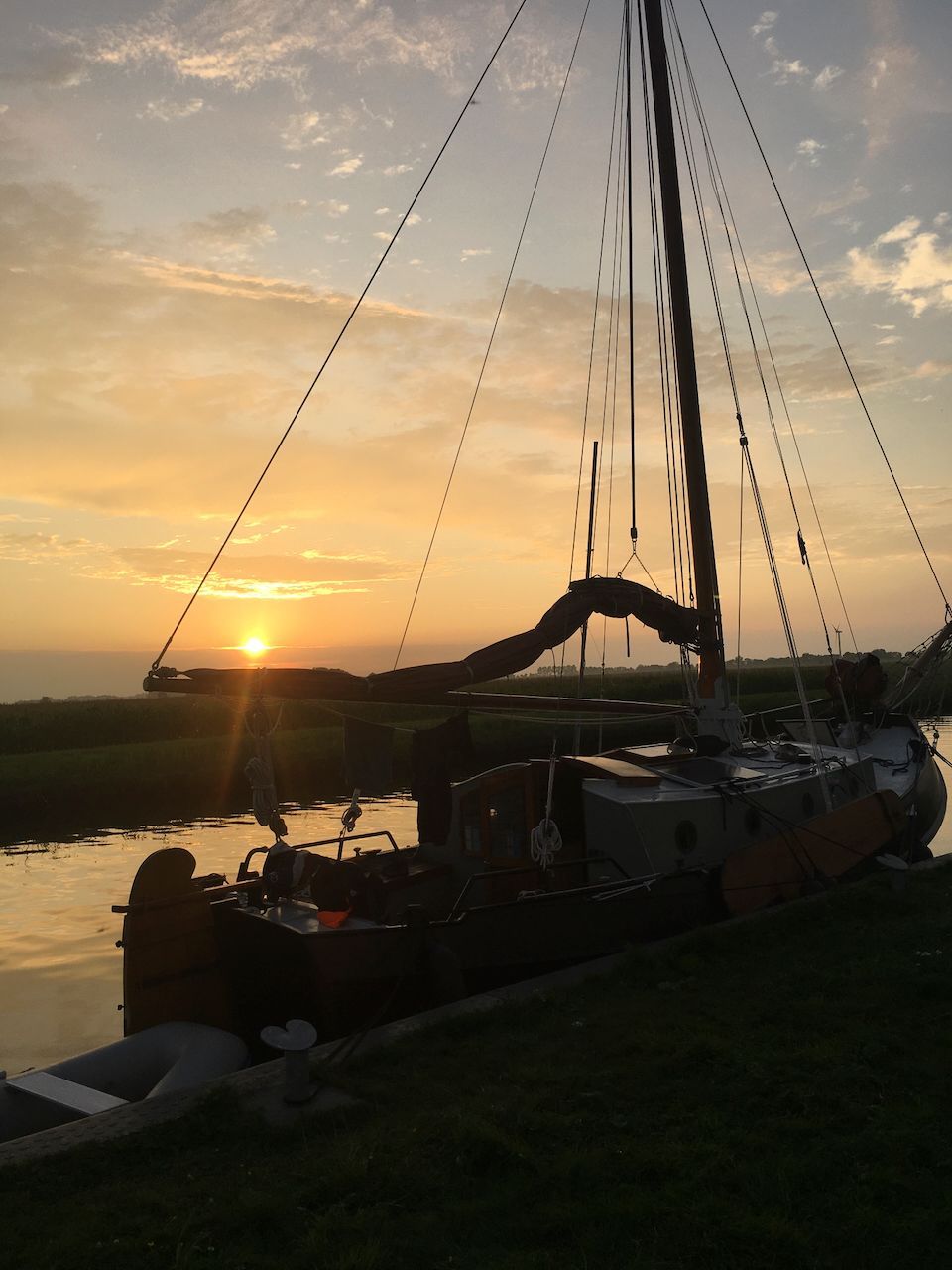 De Wijde Blik tegen de zonsondergang op het kalme water, met een warme oranje lucht en weerspiegelingen op het meer.