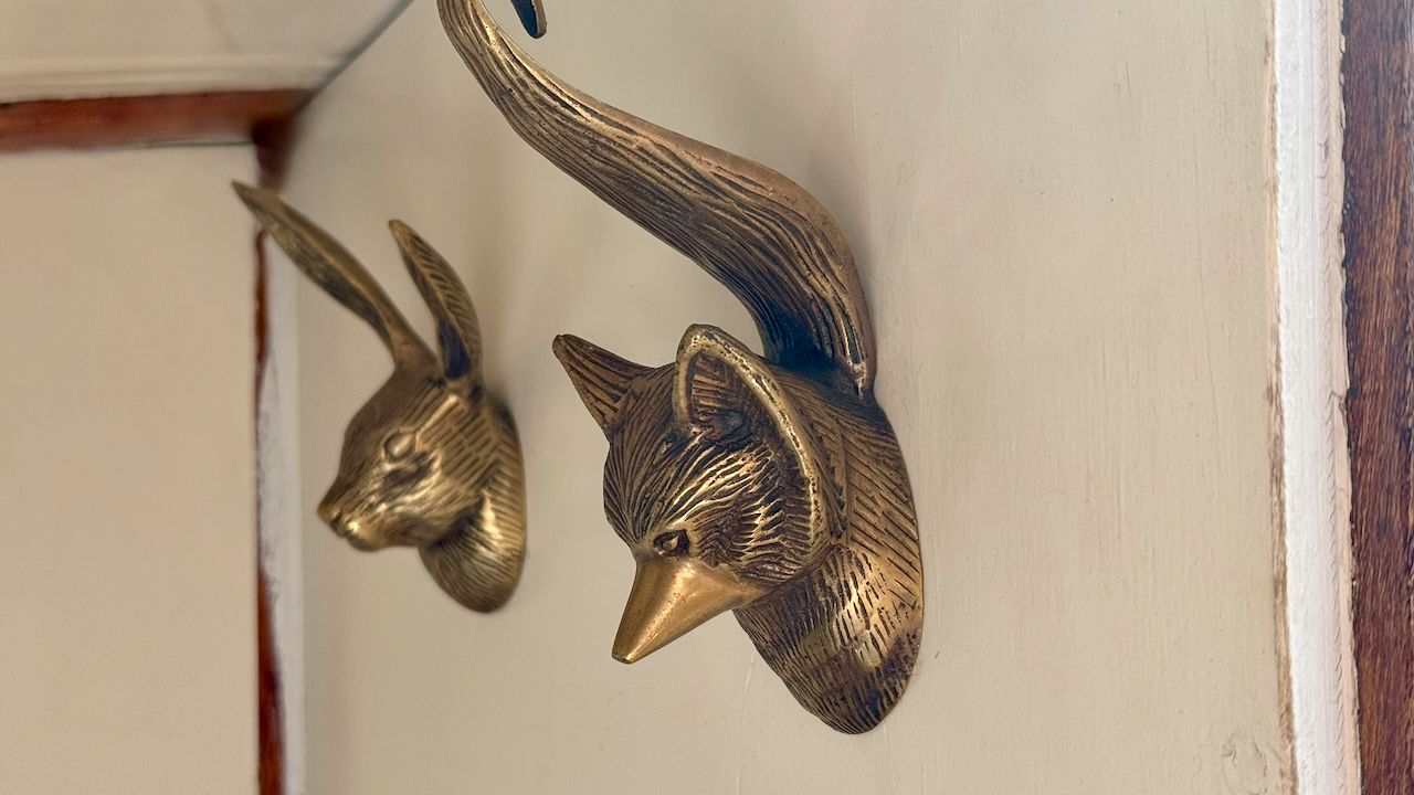 Twee bronzen dierenkoppen aan de muur als kapstok