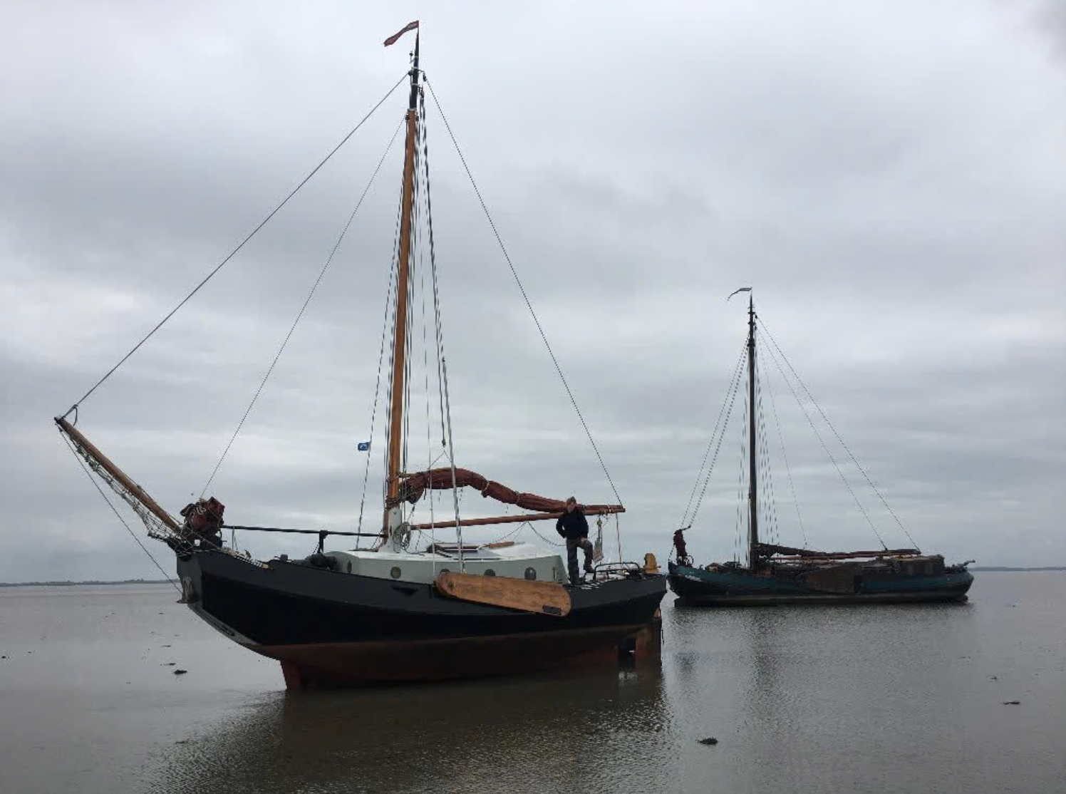 Twee zeilboten liggen aangemeerd op kalm water onder een grijze, bewolkte hemel.