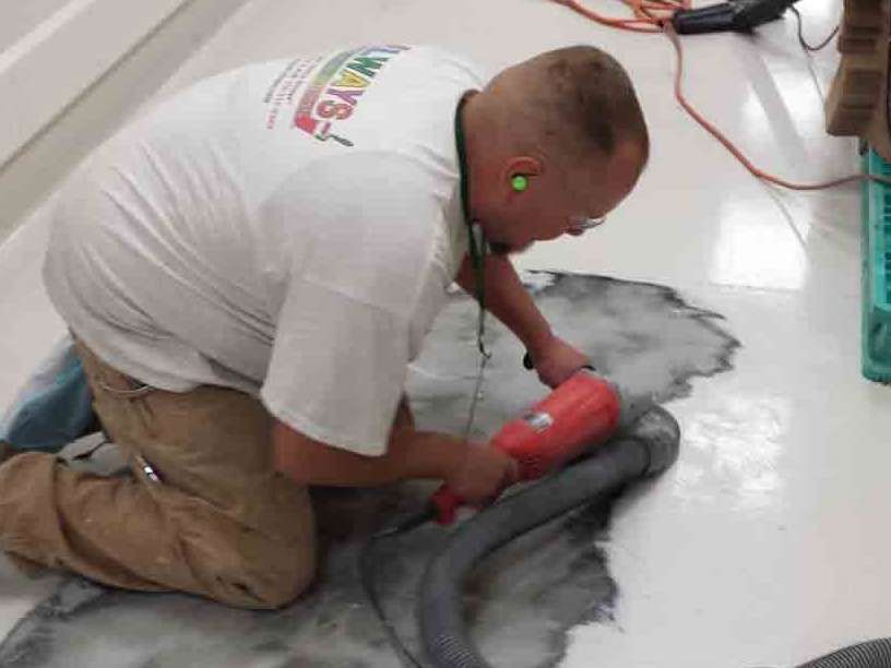A man is kneeling on the floor using a vacuum cleaner.