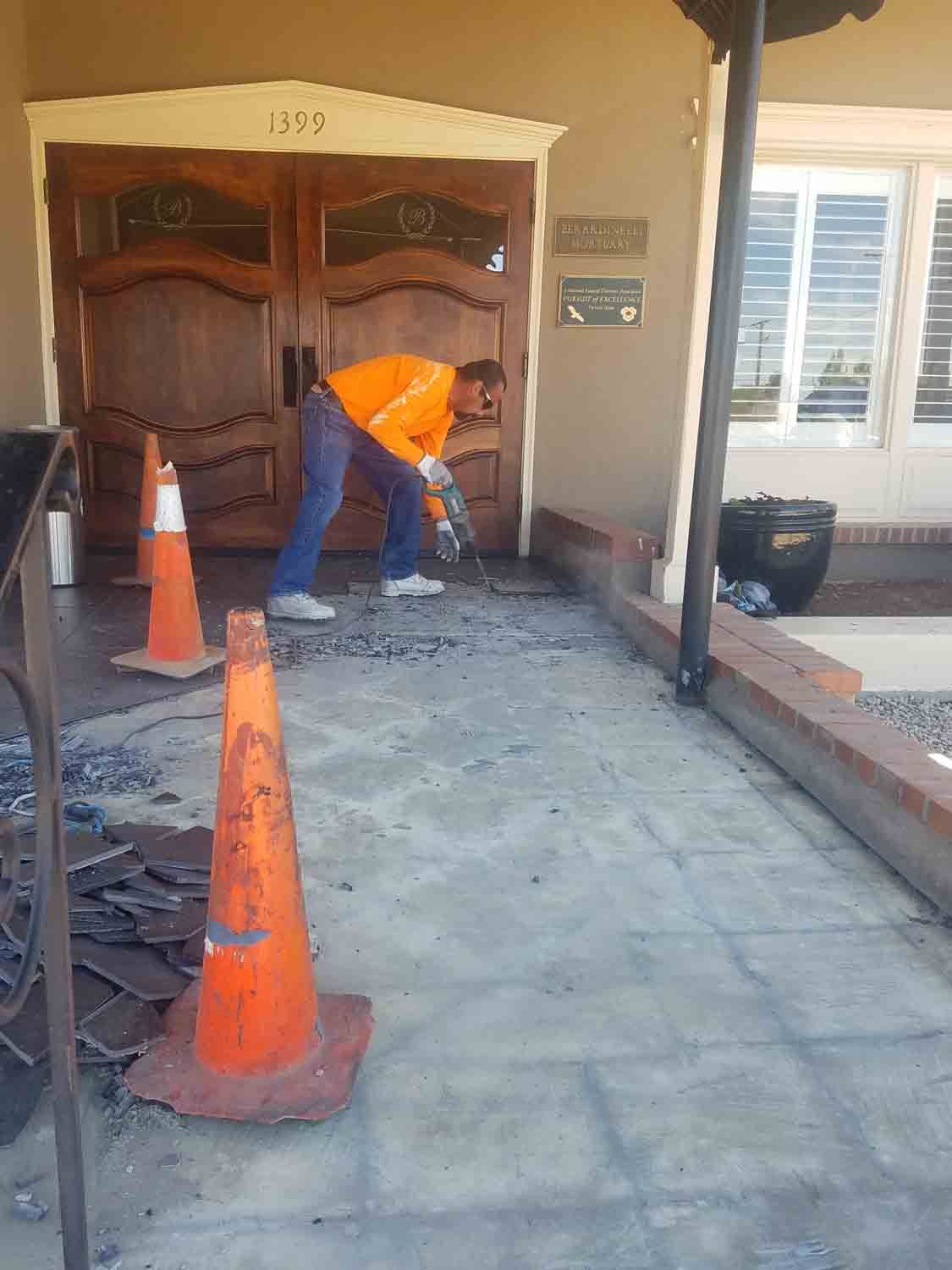 A man is working on a sidewalk in front of a building.