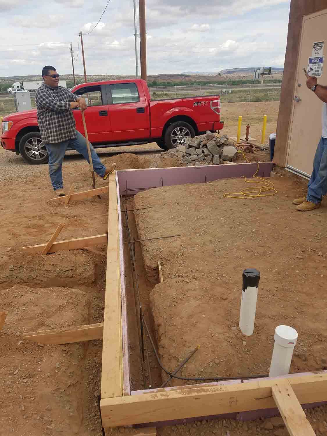 A man is standing next to a red truck in a dirt field.