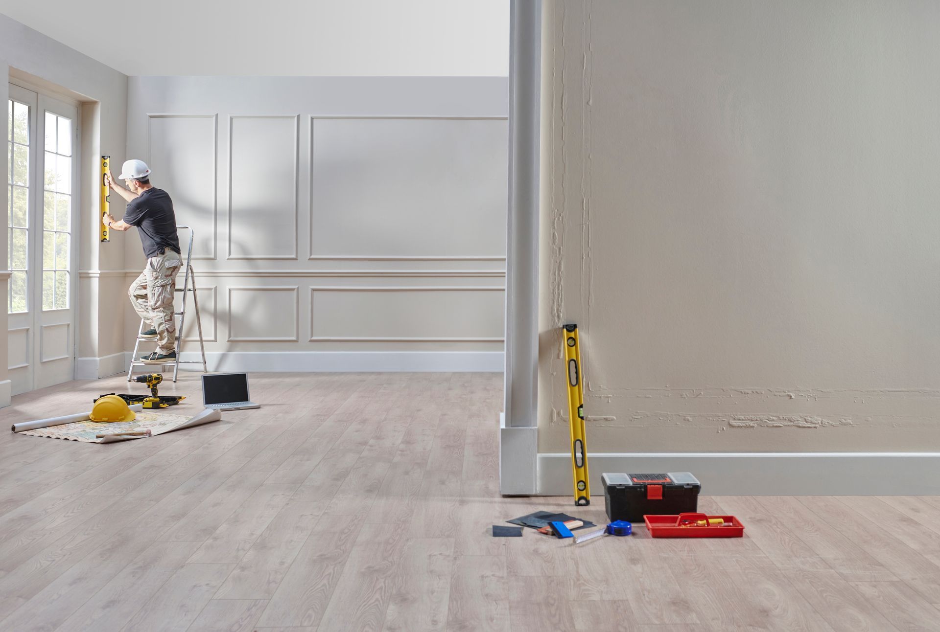 Painter in white uniform working in a bright room with paint supplies and tools on the floor.