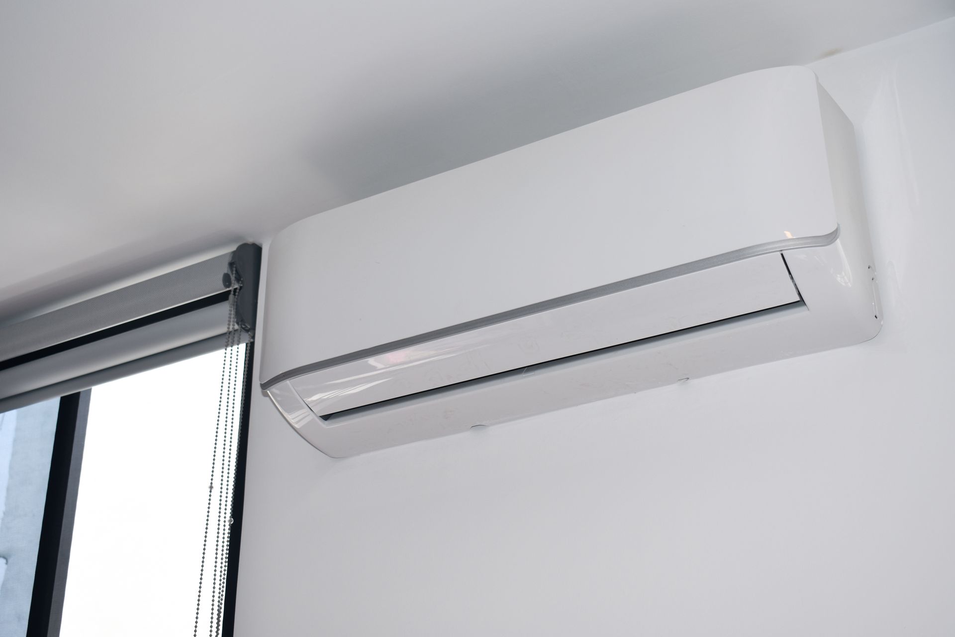 Wall-mounted white air conditioner above a window in a bright room