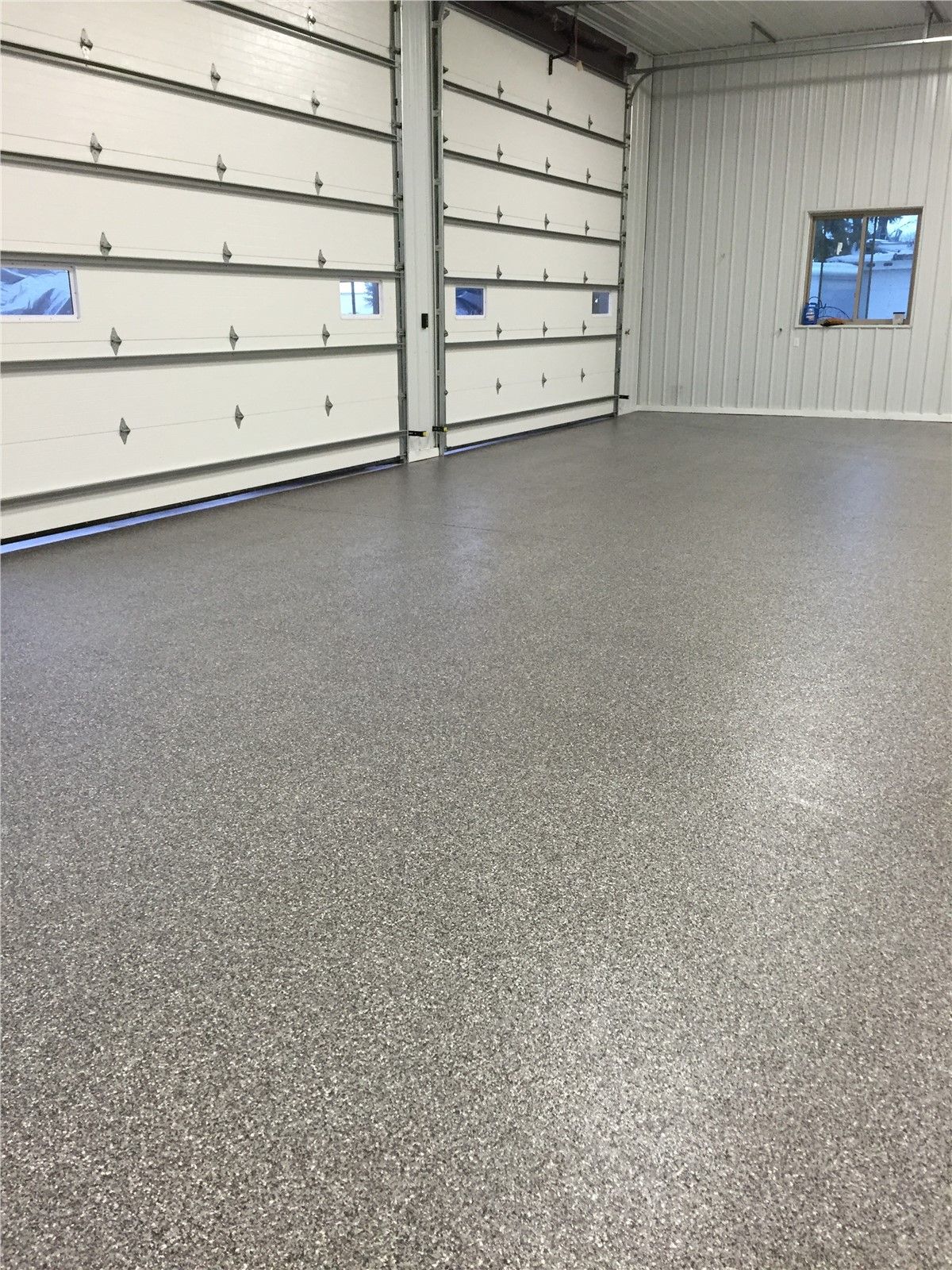 A garage with a gray floor and white garage doors.