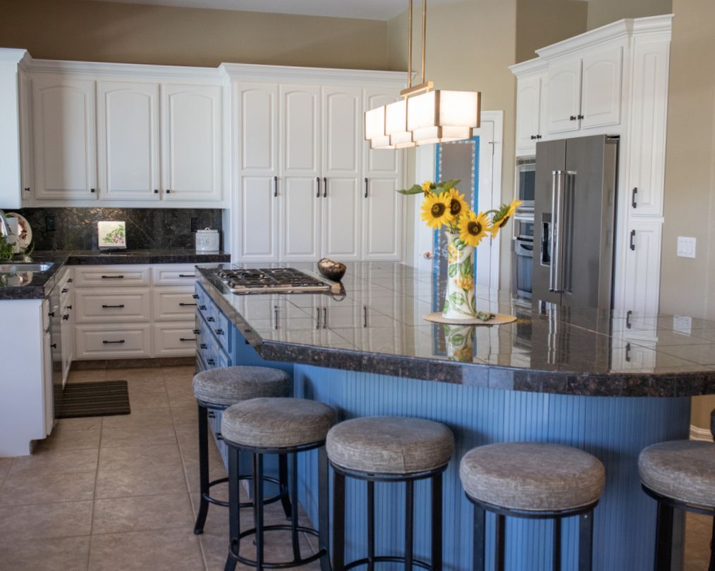 A kitchen with a blue island and stools and a vase of sunflowers on the counter.