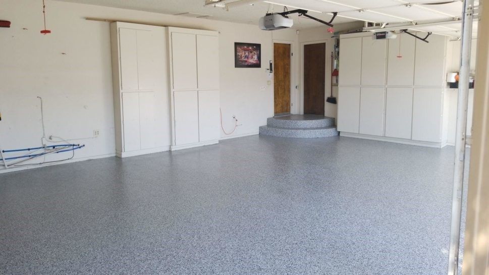 An empty garage with a gray floor and white cabinets.