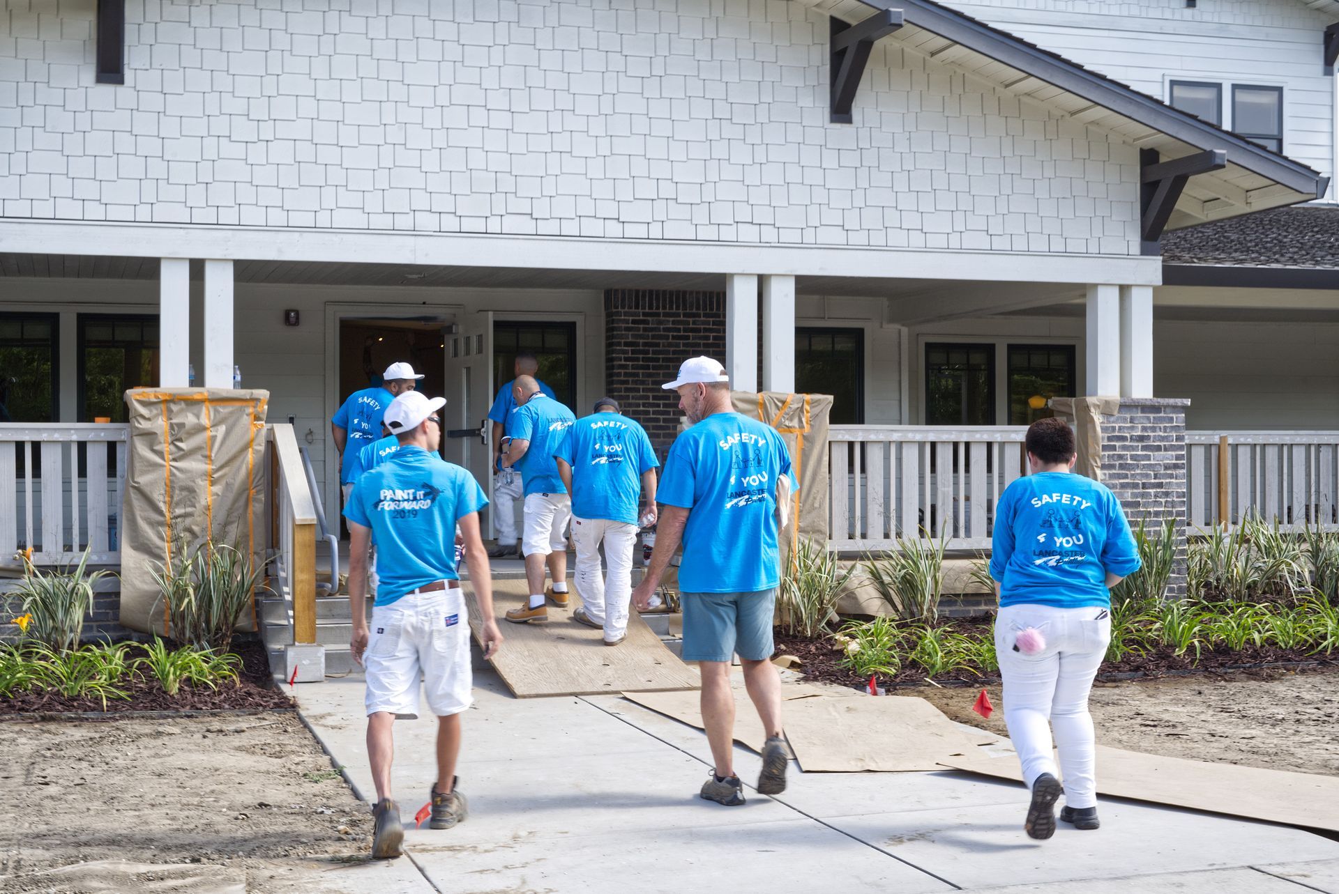 A group of people in blue shirts are walking in front of a house.