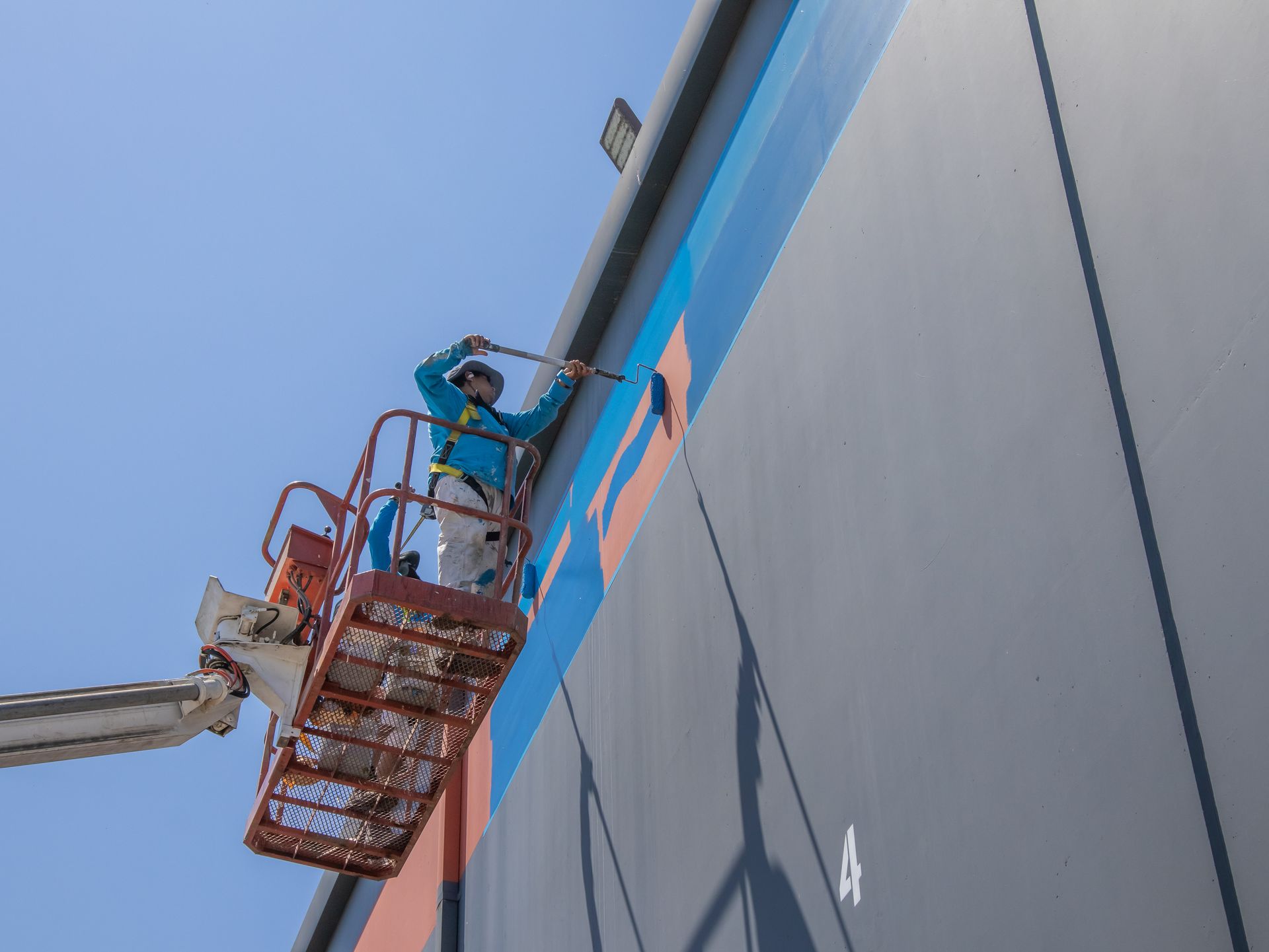 A man is painting the side of a building with a crane.