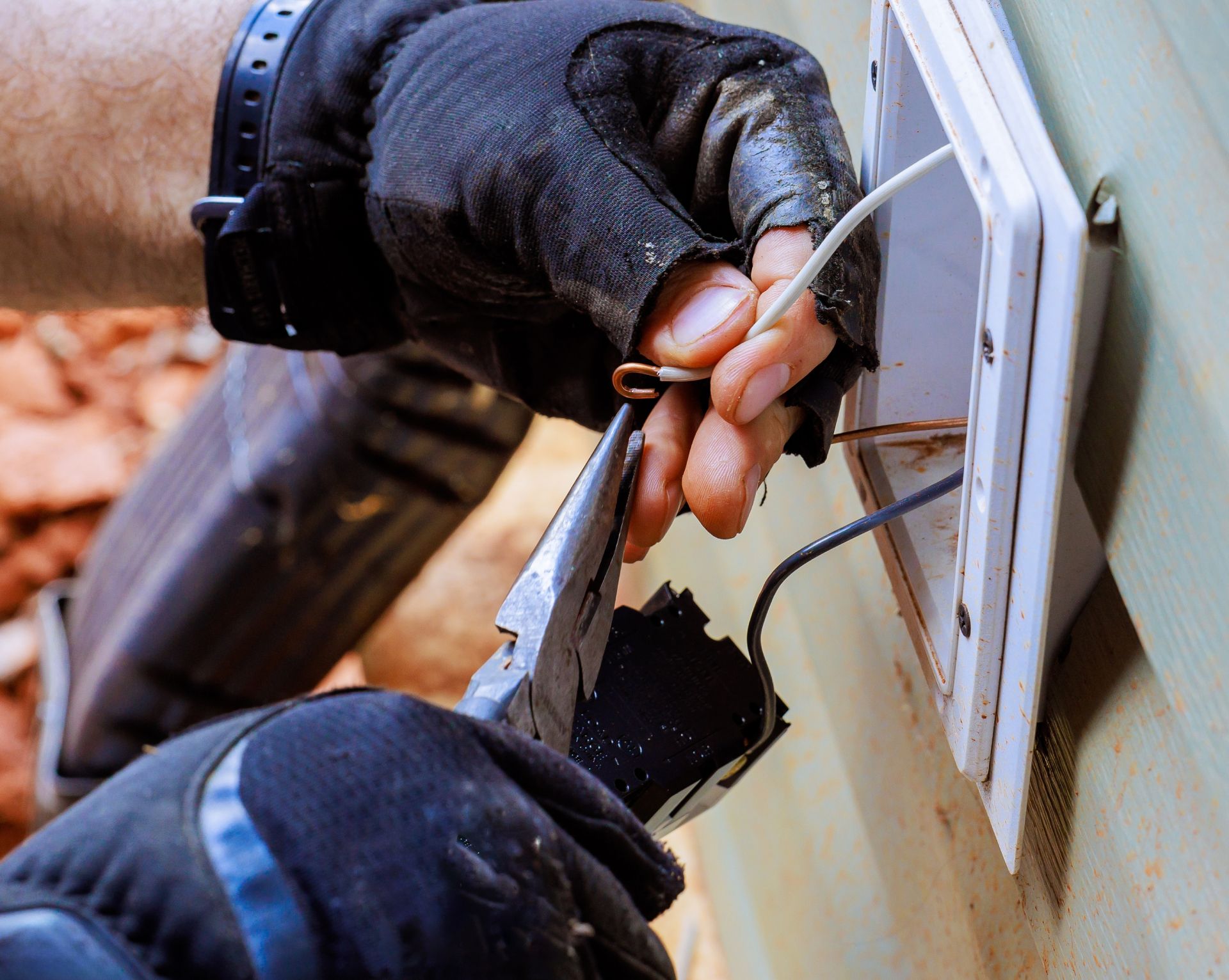 Gloved hands using a screwdriver to pry open a white wall panel or window frame