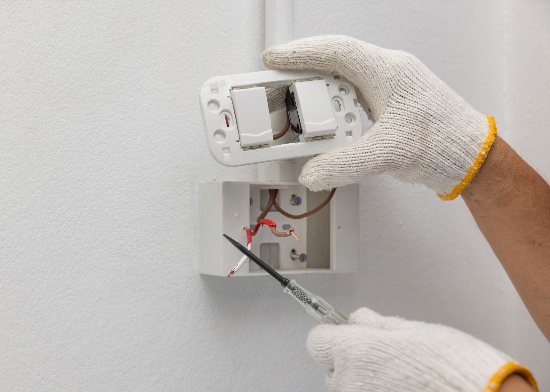Gloved hands wire a wall thermostat at an open electrical box.