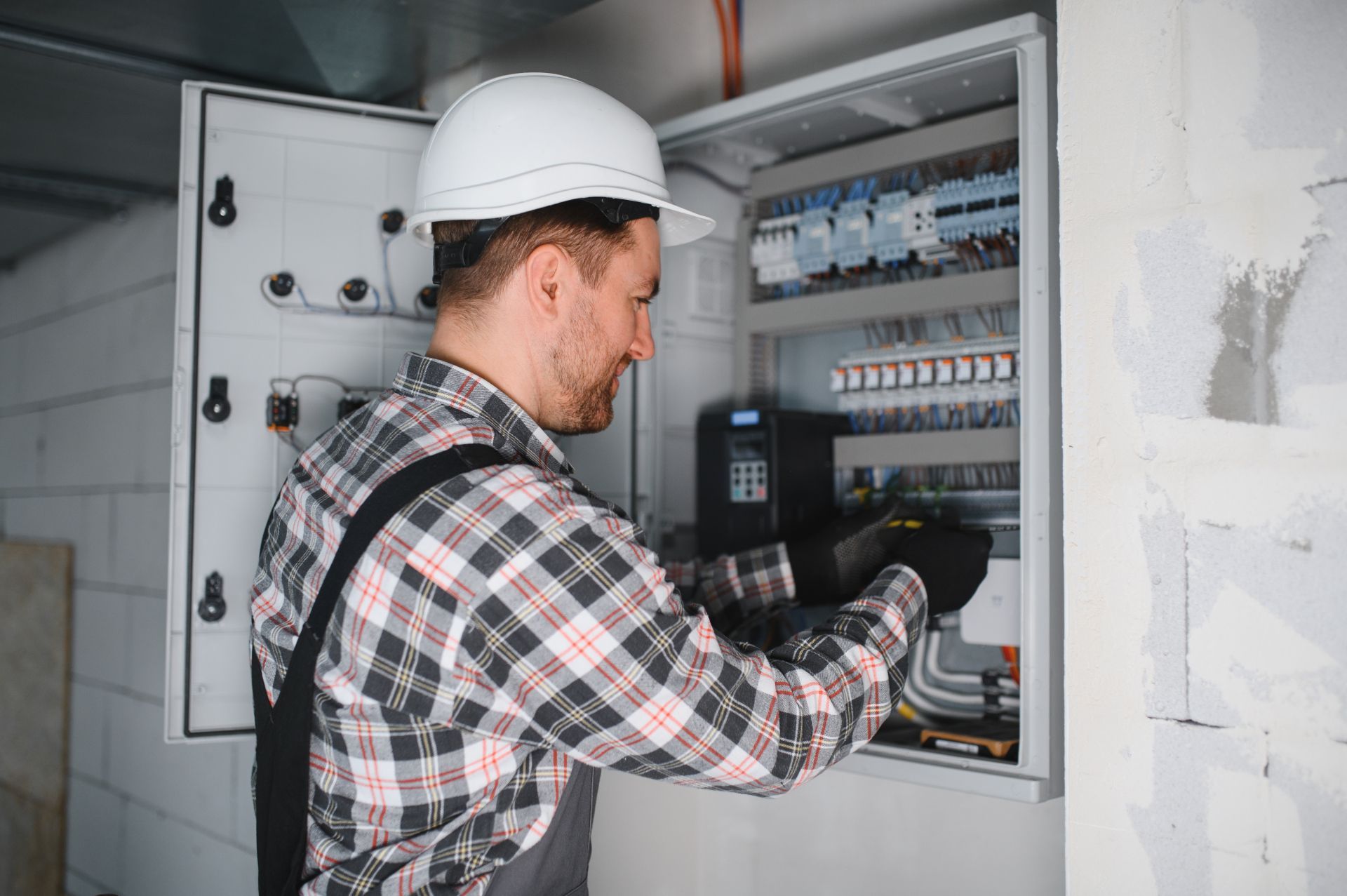 Electrician working inside an open wall electrical panel with tools and wiring.