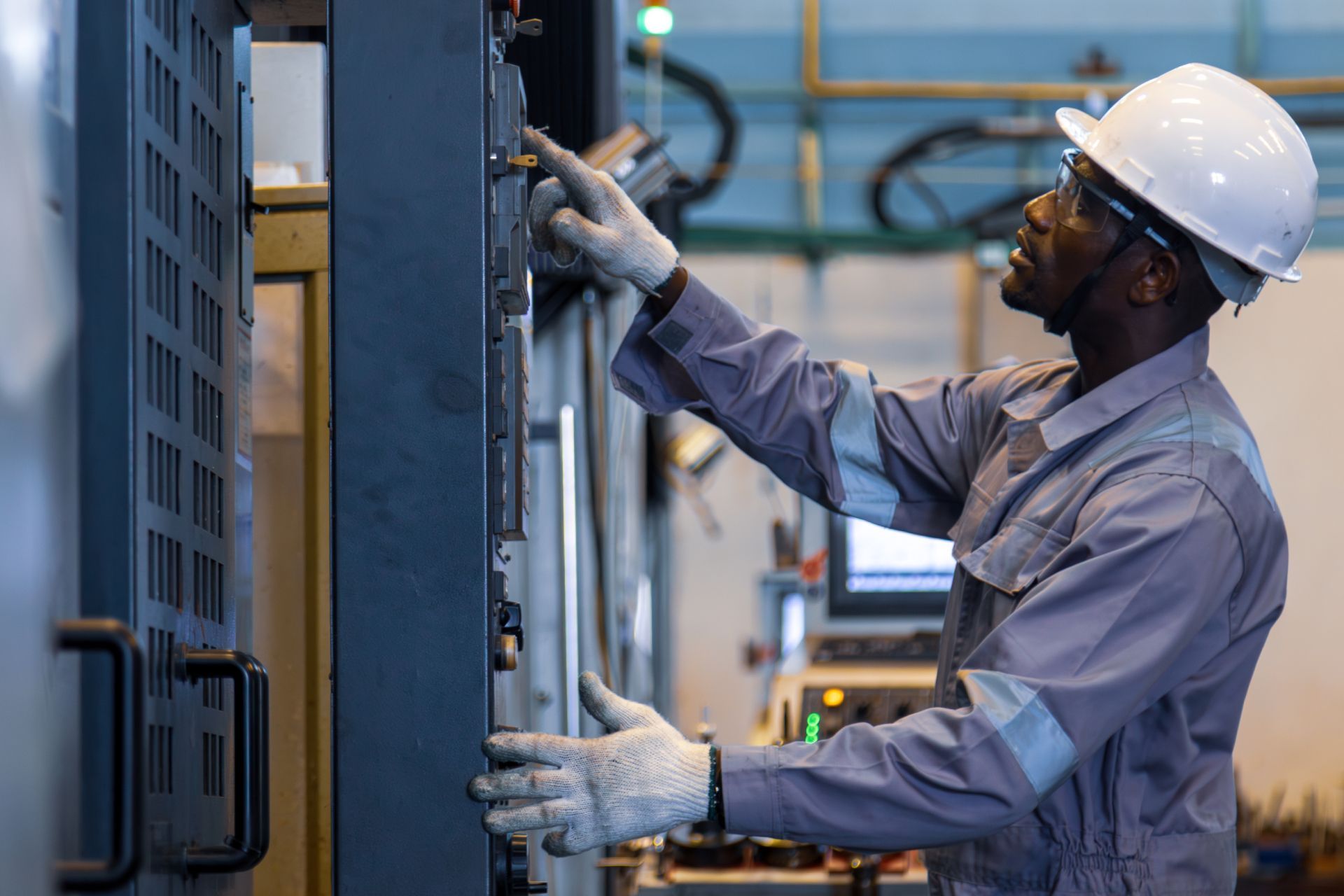Worker in hard hat inspecting electrical control panel in an industrial facility