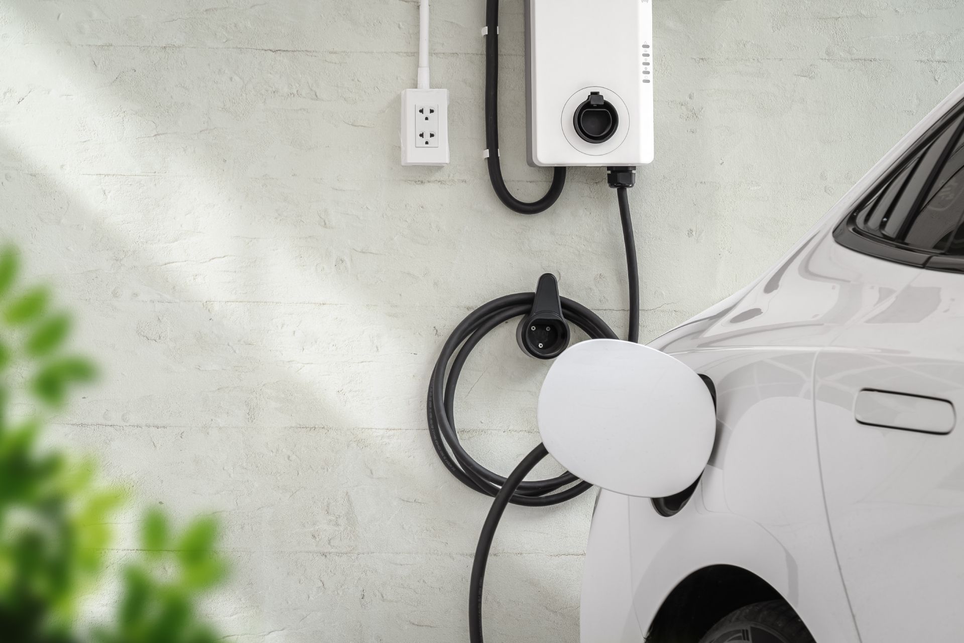 Electric car charging in a garage, with a wall charger connected to a white vehicle.