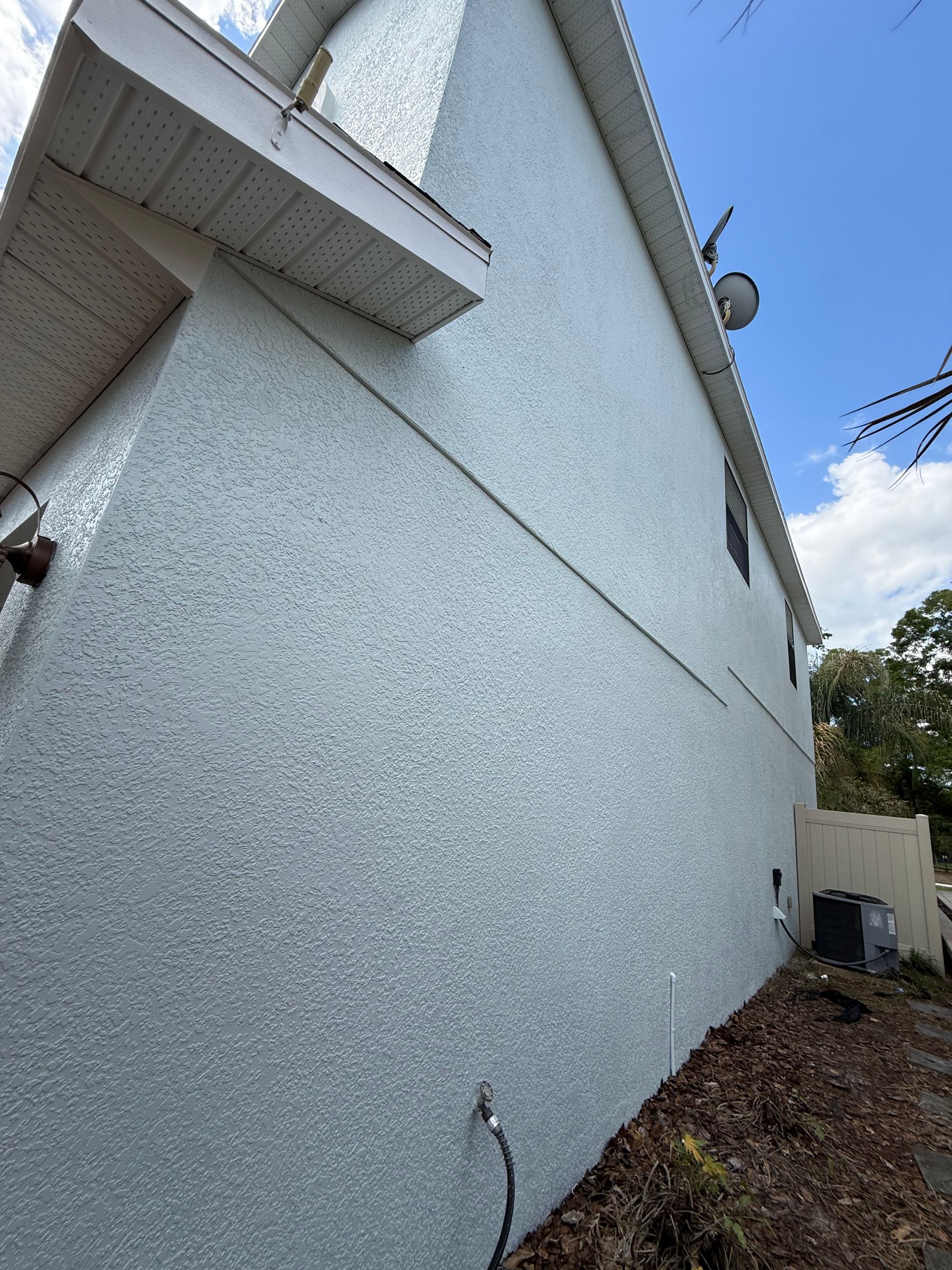 Professional exterior painting in a narrow side yard using precision techniques on a two-story stucco home in DeLand, FL