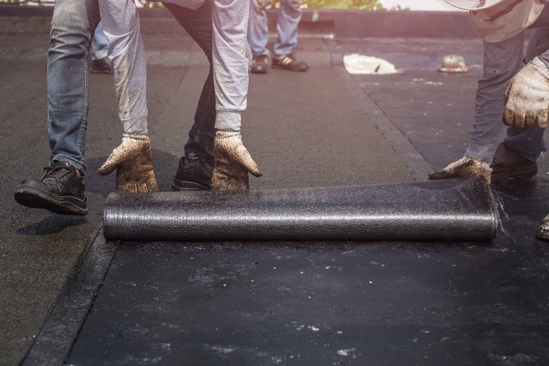 Roofers rolling out a black roofing membrane on a flat roof.